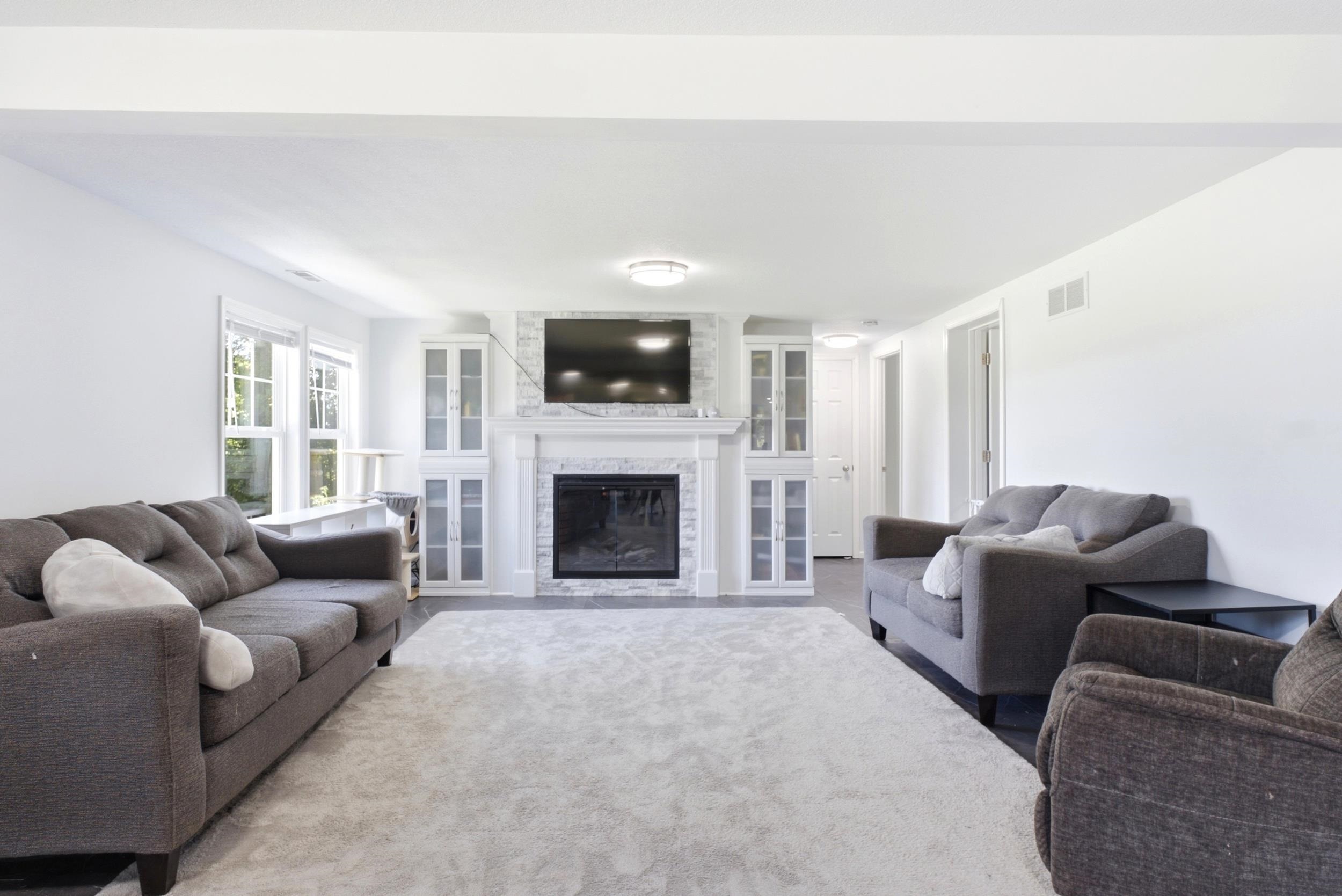 Living area featuring a central fireplace with a stone surround, white mantel, and built-in cabinetry