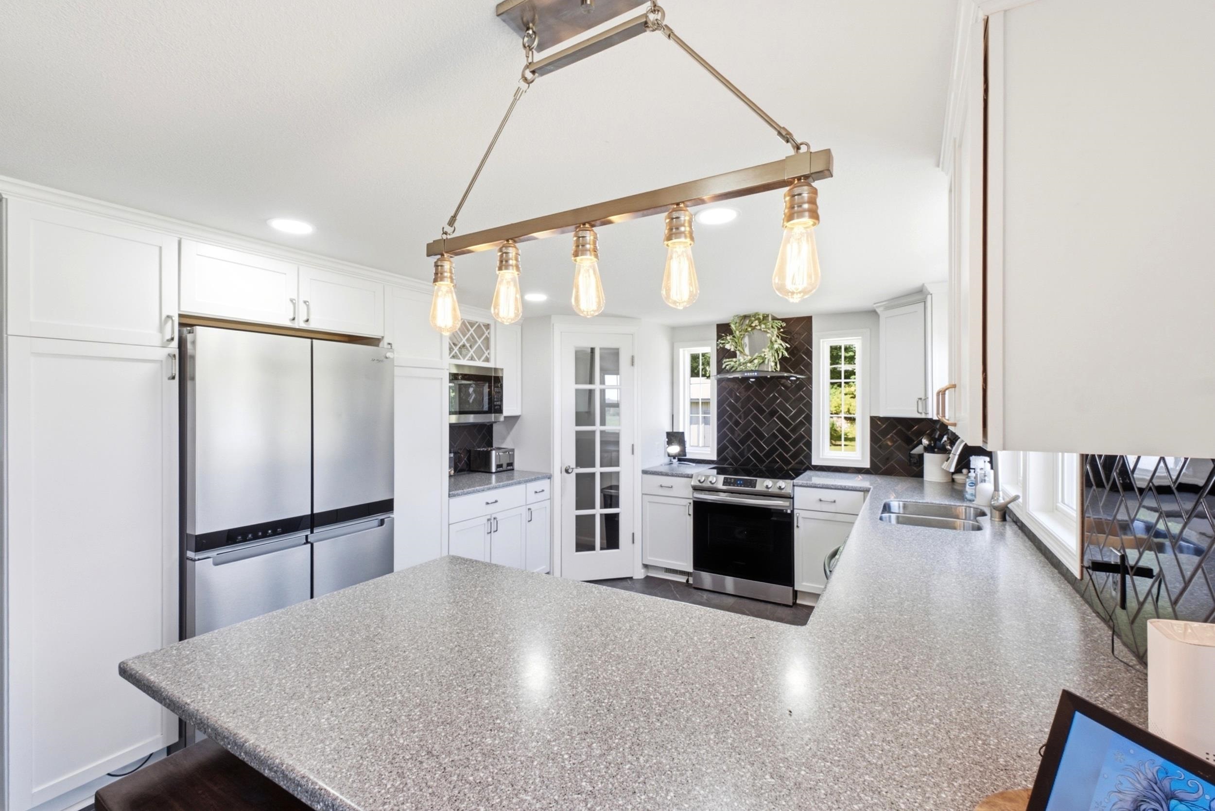 Spacious kitchen featuring an expansive island with speckled countertops, white cabinetry, and stainless steel appliances