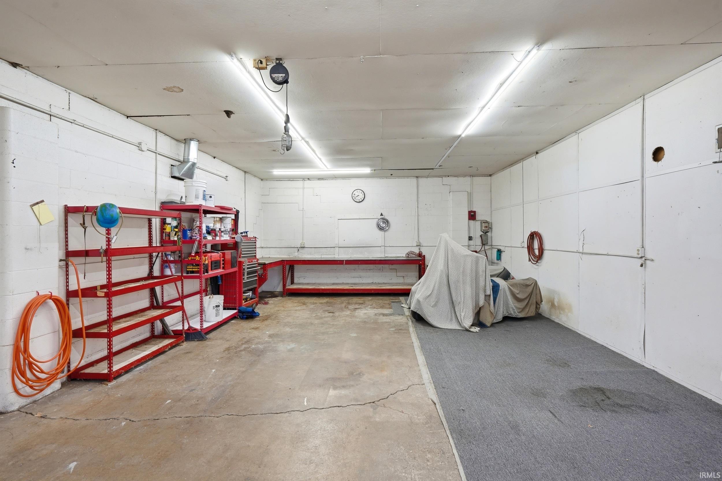 Spacious utility room featuring a concrete floor, white panel walls, and bright overhead fluorescent lighting