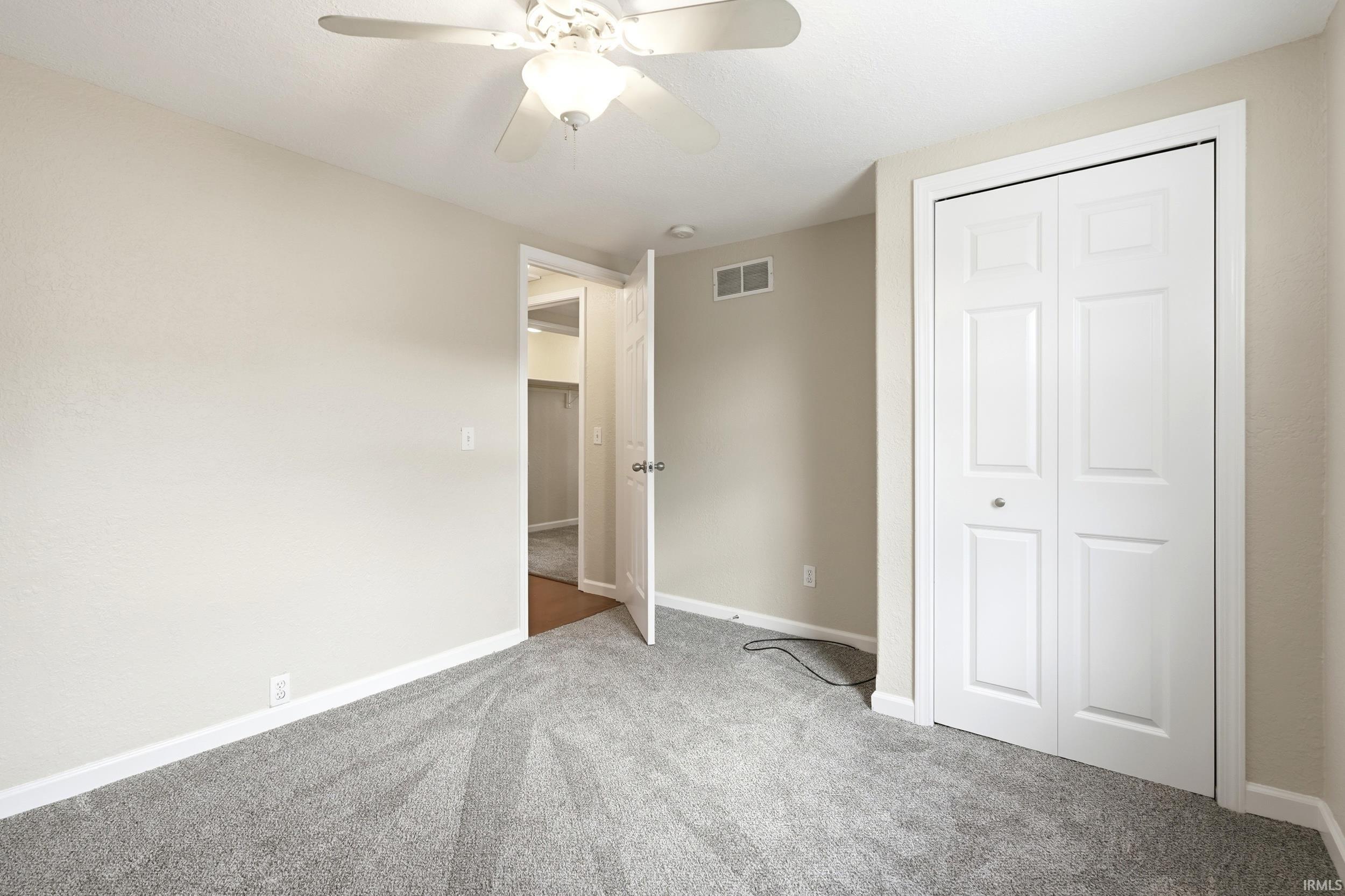 Carpeted room featuring neutral wall tones, a ceiling fan with integrated lighting, white bi-fold closet doors, and white trim