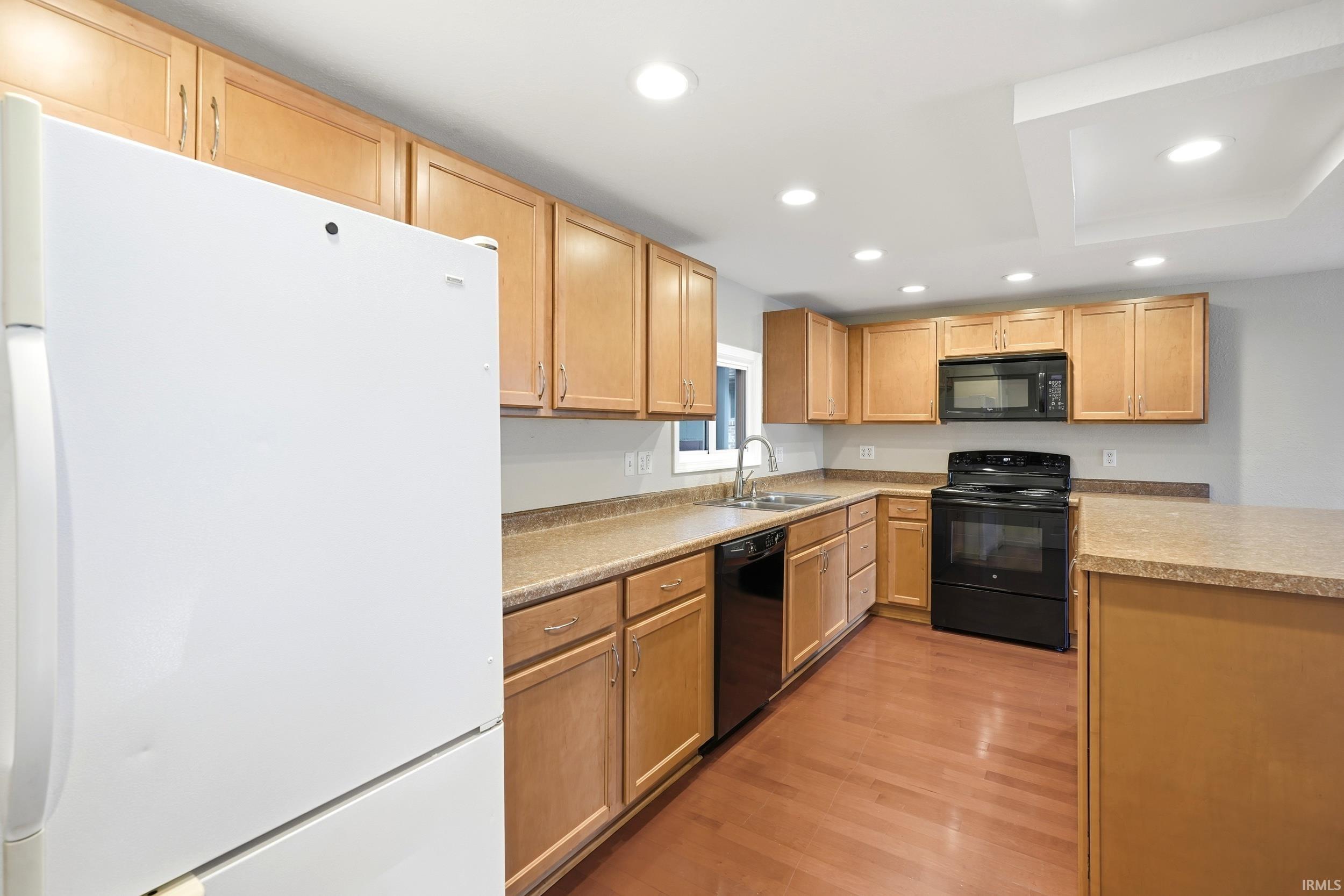Kitchen featuring extensive light wood-finish cabinetry, black appliances, laminate countertops, and wood-finish flooring