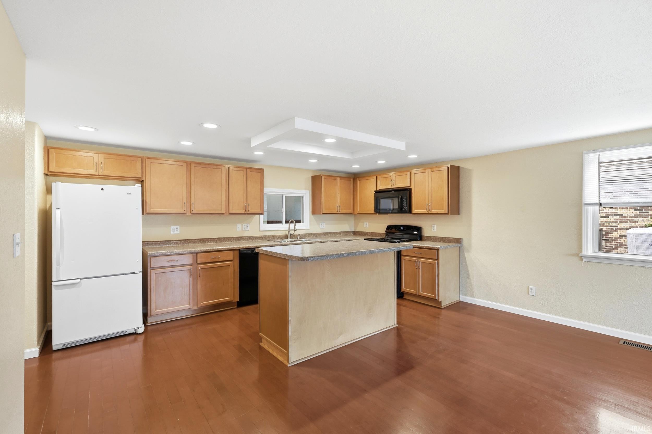 Spacious kitchen featuring wood-finish flooring, light wood cabinetry, and a central island with a light-toned countertop