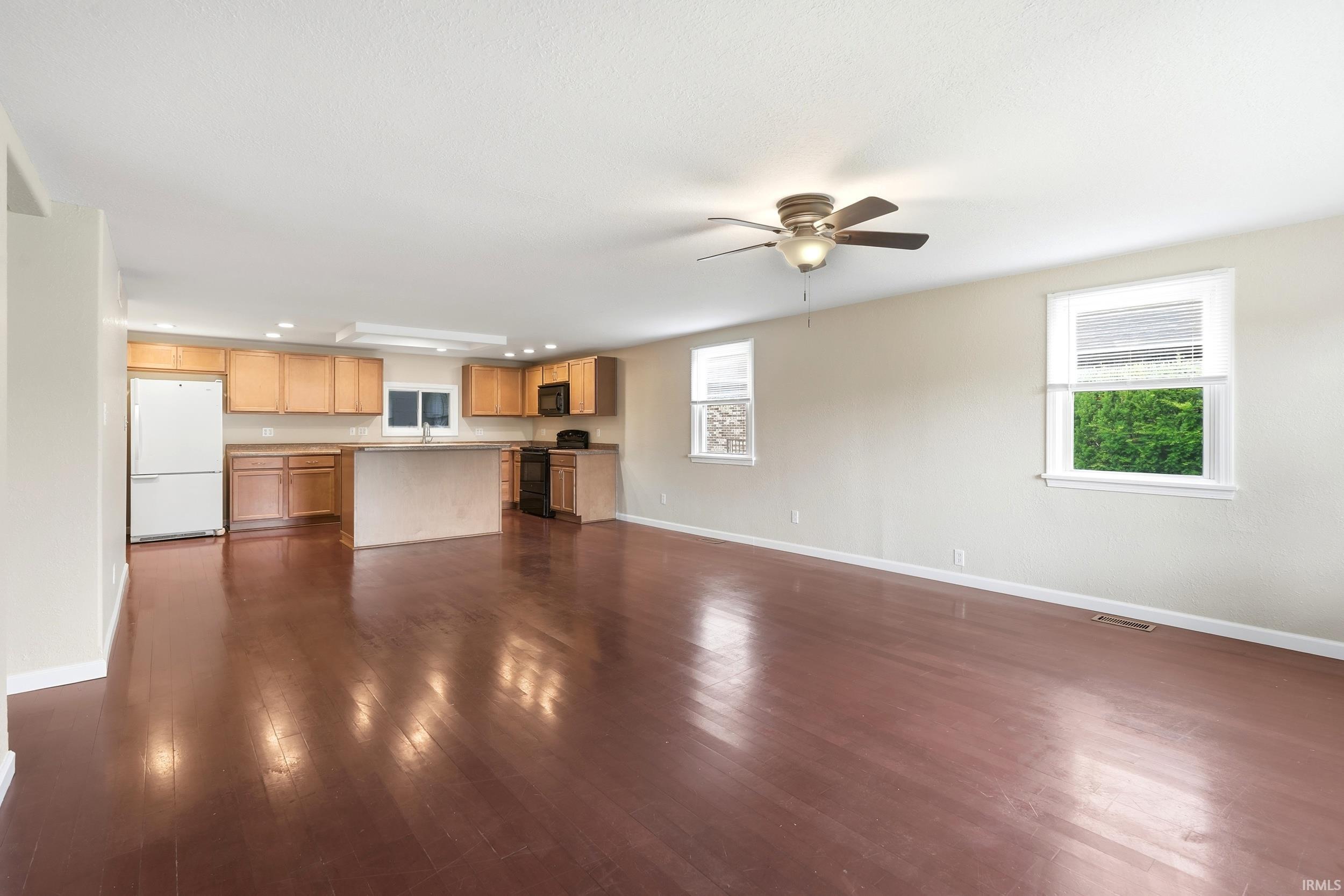 Expansive living area with wood-finish flooring, a ceiling fan, and multiple windows