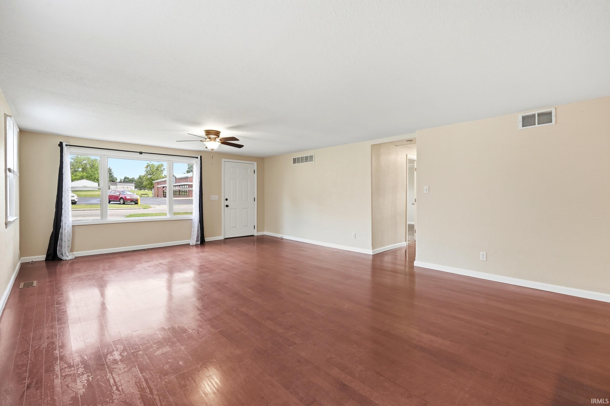 Spacious living area featuring wood-finish flooring, a ceiling fan, and a large front window