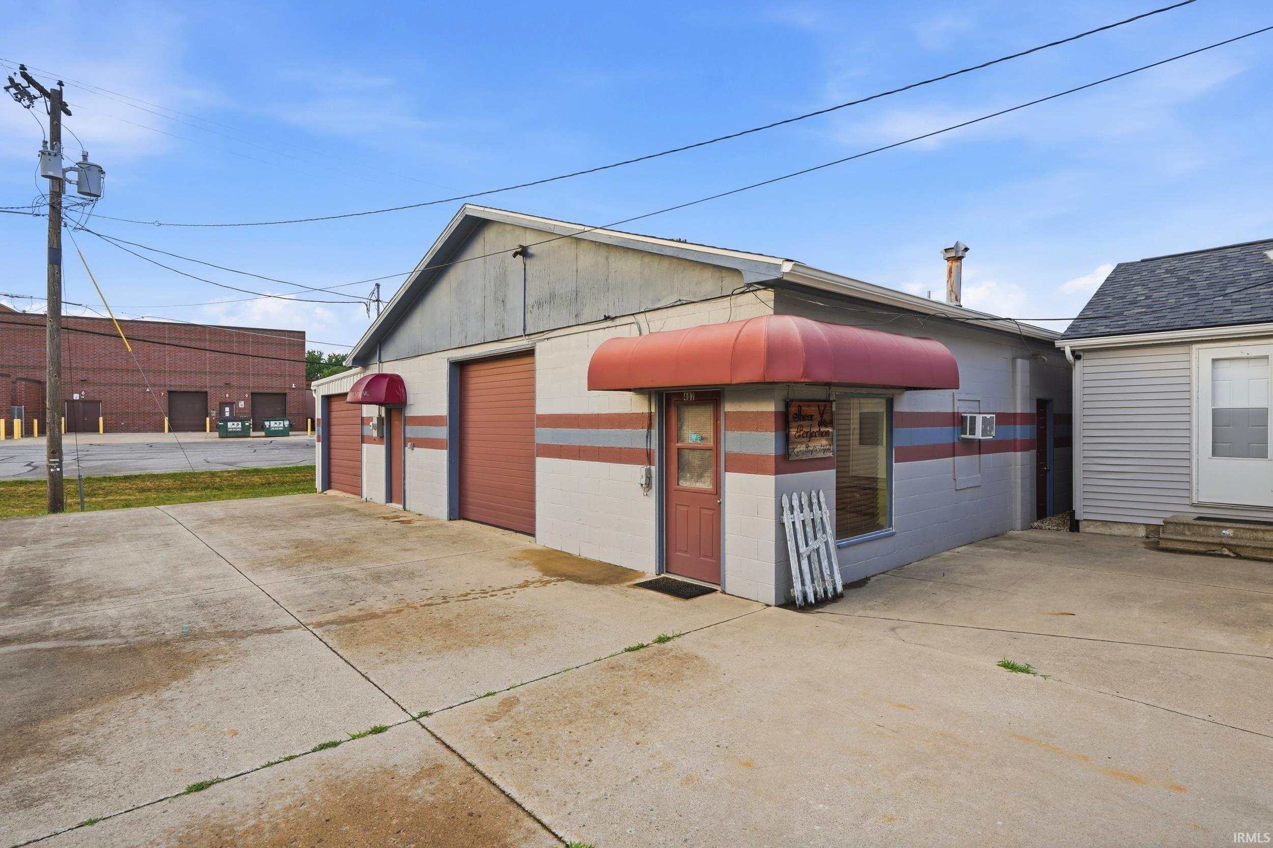 Commercial building featuring two overhead garage doors, a pedestrian entry, and red awnings