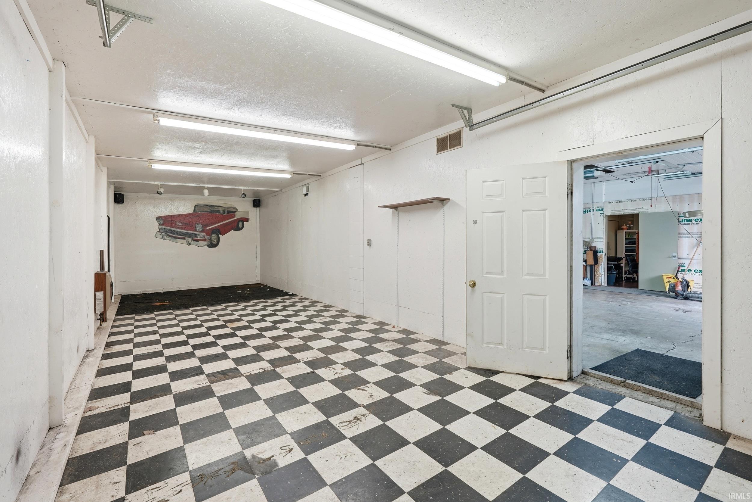 Spacious interior room featuring checkerboard flooring, white paneled walls, and fluorescent lighting