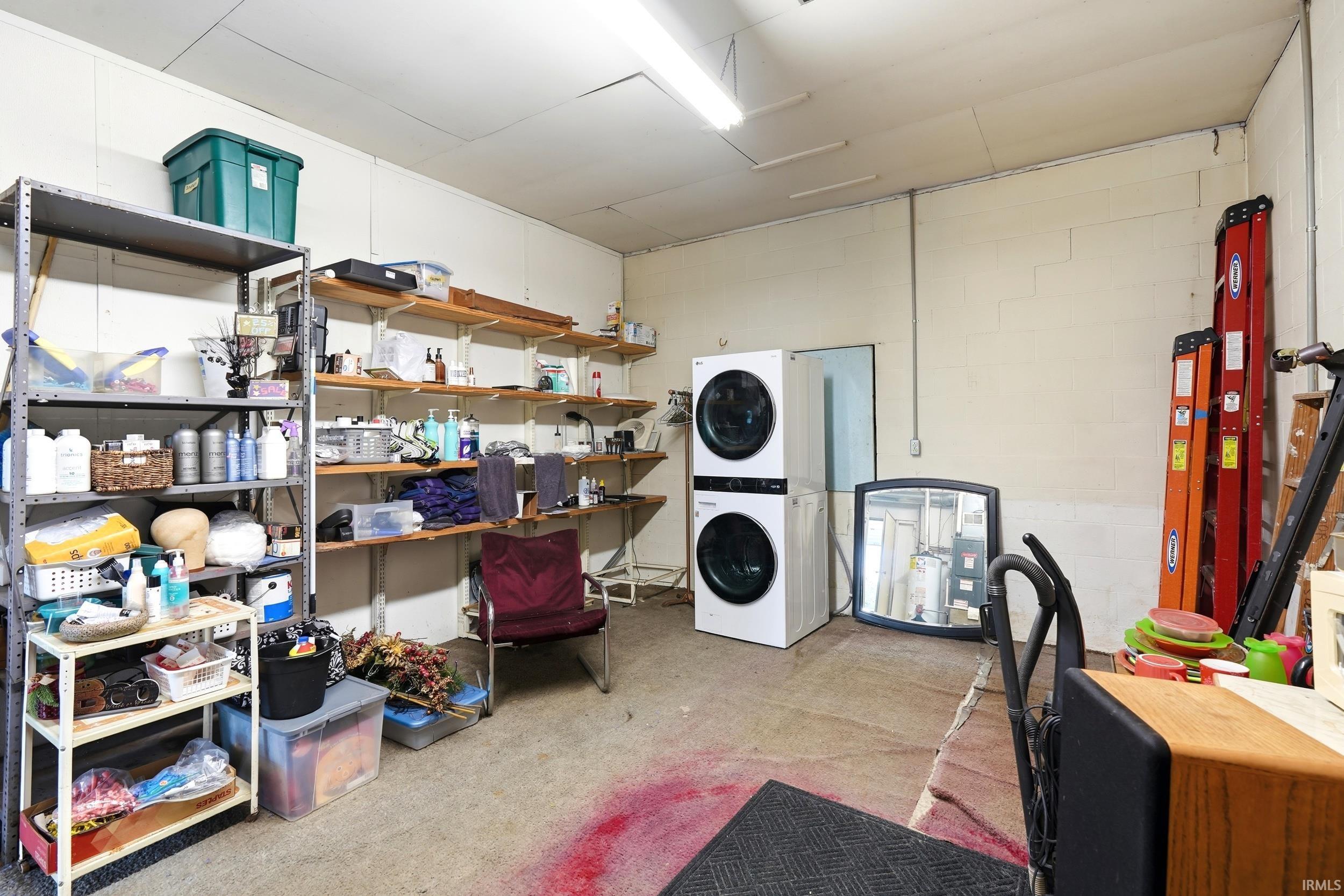 Utility room featuring a stacked washer and dryer unit, ample wall-mounted shelving, and bright overhead lighting