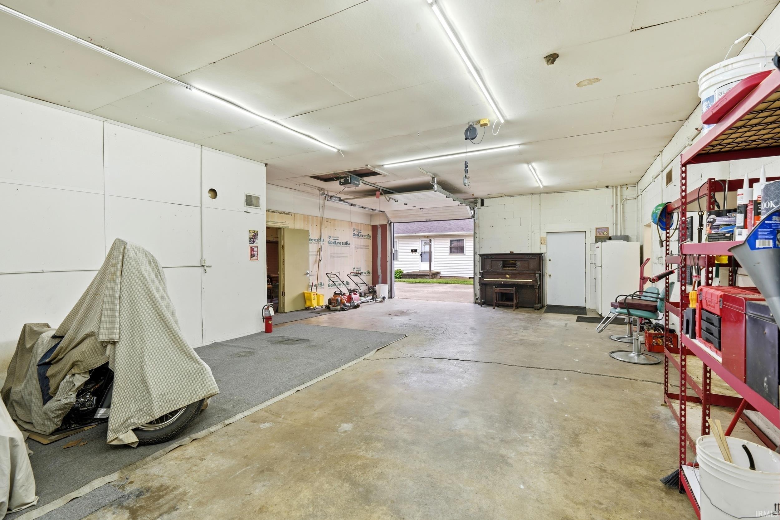 Spacious interior featuring a concrete floor, overhead fluorescent lighting, exposed ceiling joists, and a garage door opening