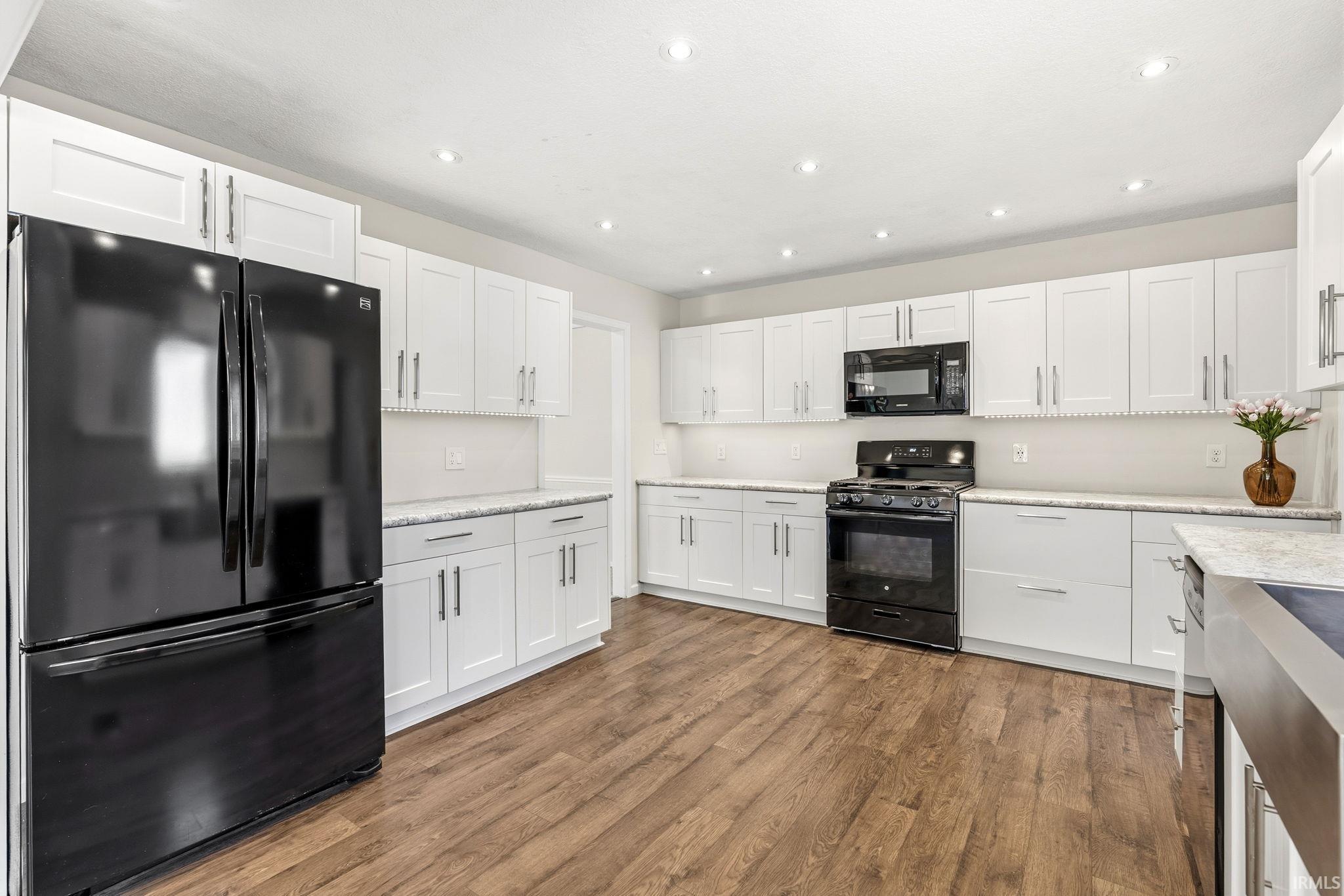 Contemporary kitchen featuring white shaker cabinetry, speckled countertops, wood-finish flooring, and recessed lighting