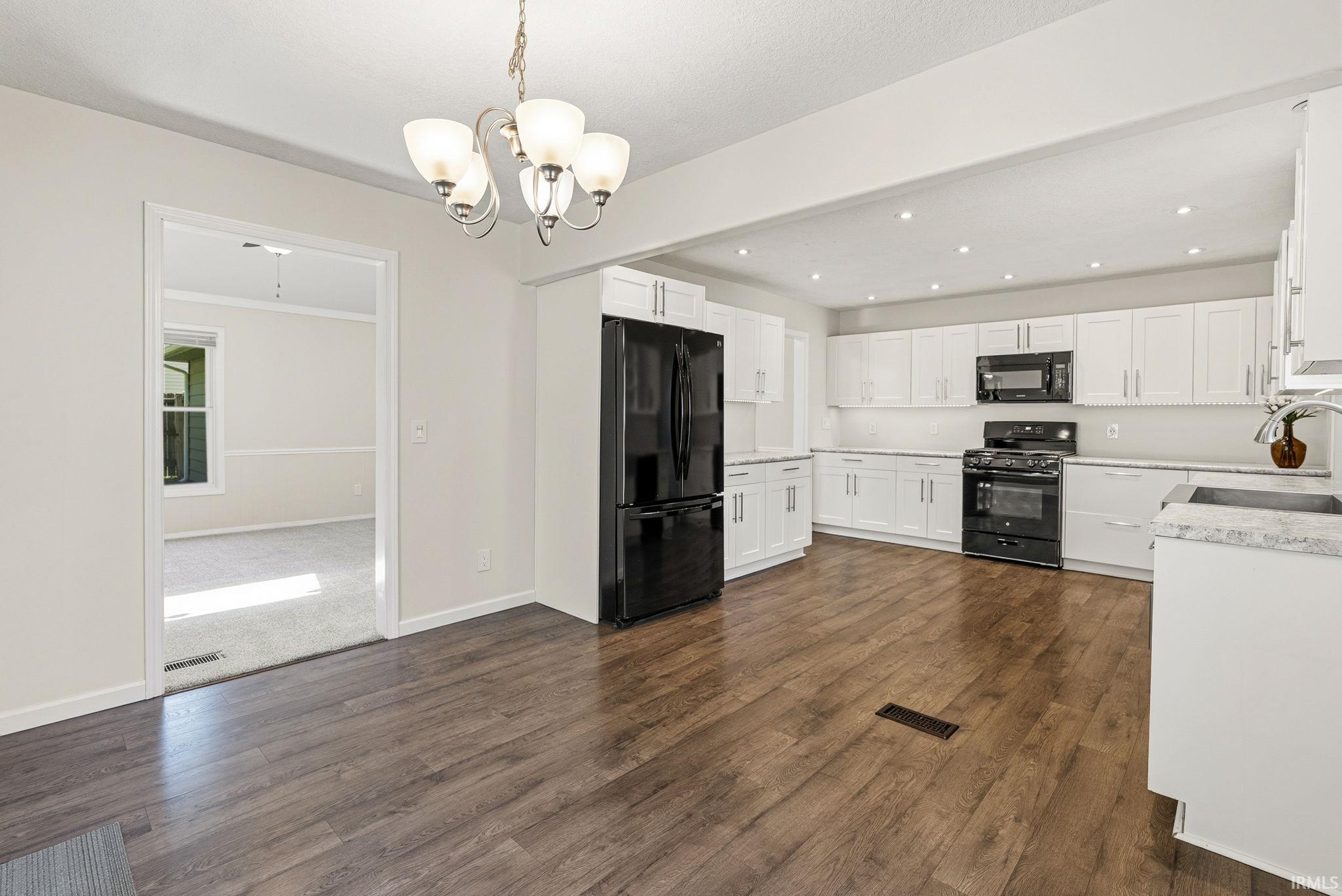 Kitchen featuring extensive white cabinetry, black appliances, light-toned countertops, wood-finish flooring, and recessed lighting