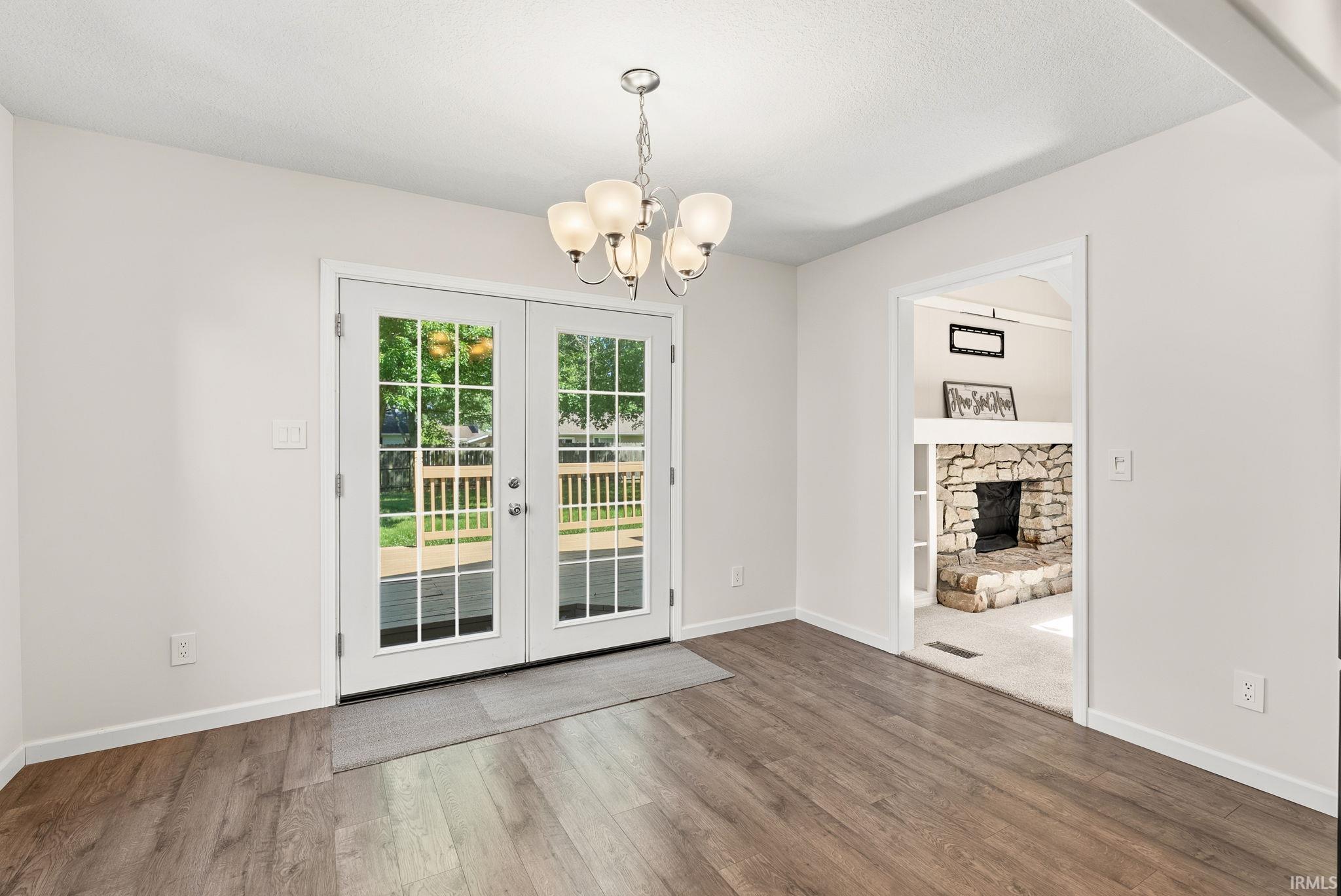 Bright dining area with wood-finish flooring, featuring a chandelier and French doors opening to a deck