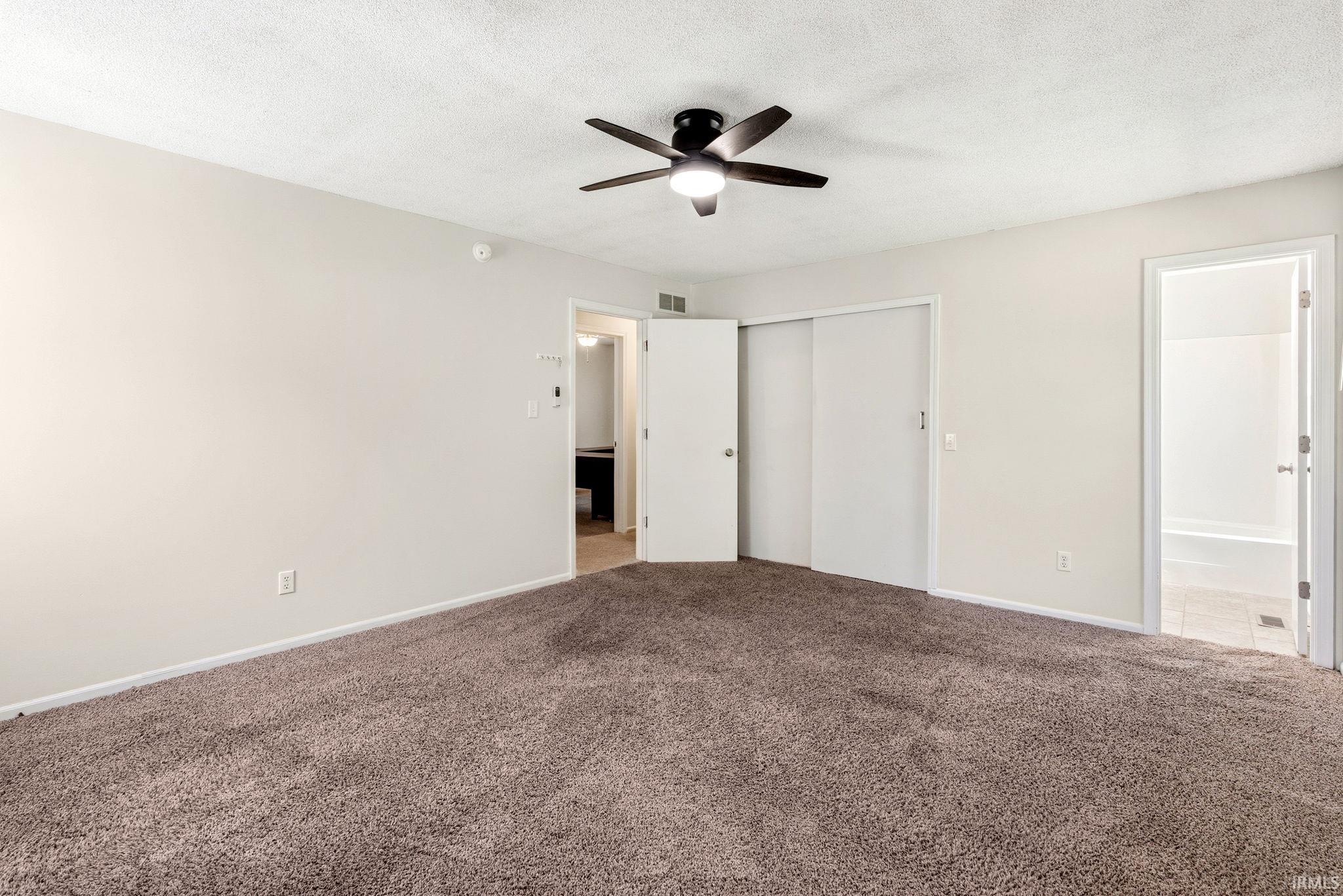 Carpeted room featuring a ceiling fan with integrated lighting, neutral wall paint, white trim, and a double sliding closet door
