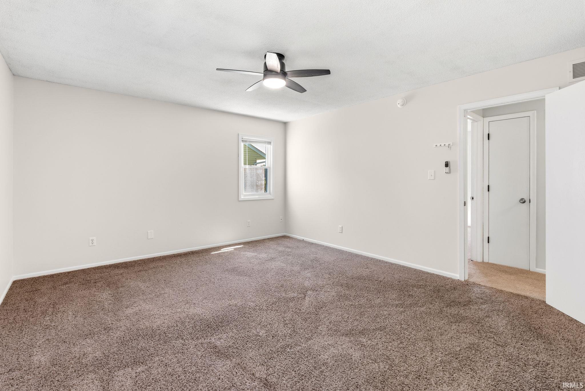 Spacious room featuring neutral carpeting, a ceiling fan with integrated lighting, and a single window providing natural illumination