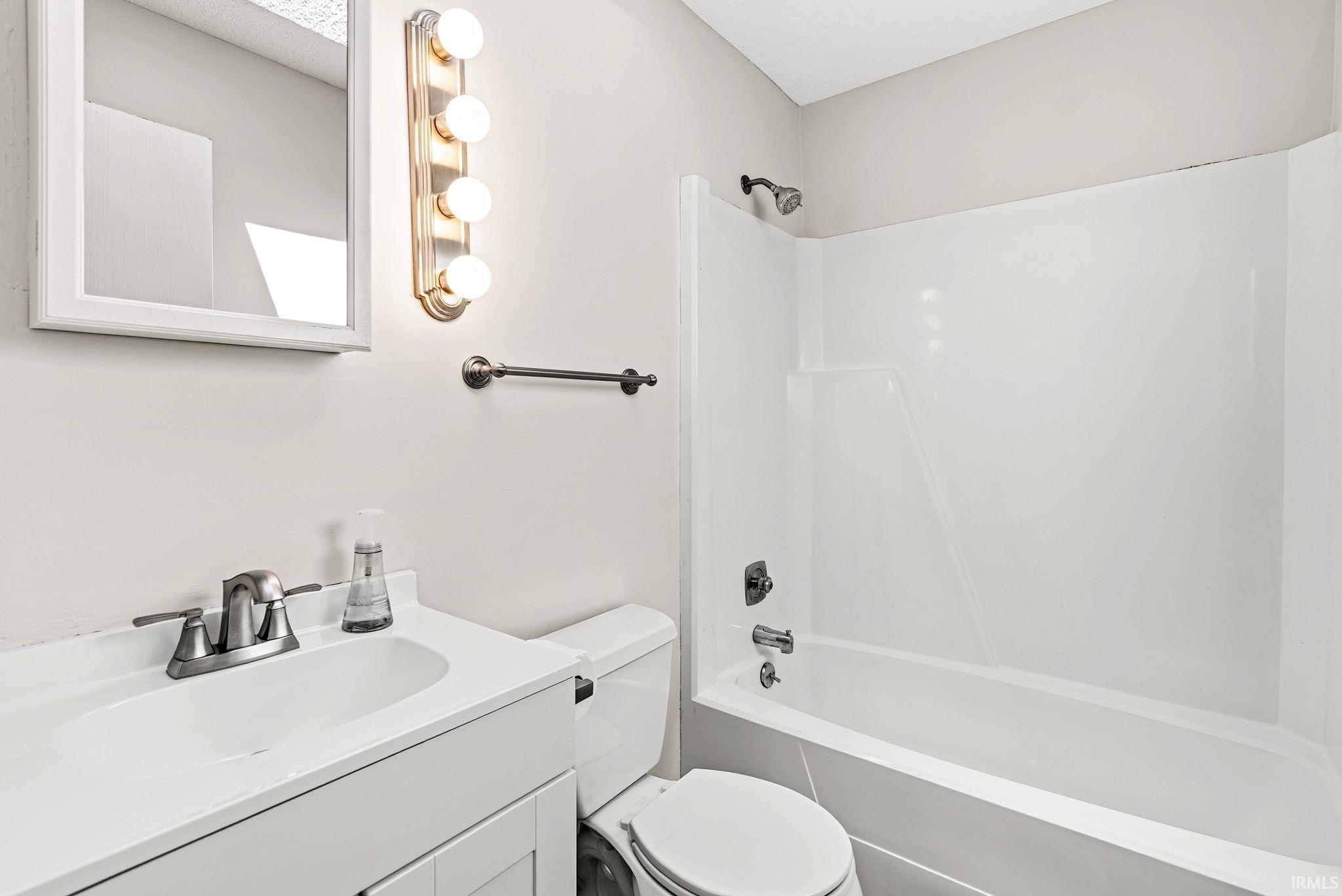 Full bathroom featuring a white vanity with integrated sink, brushed nickel faucet, framed mirror, and a full-size bathtub with shower combination