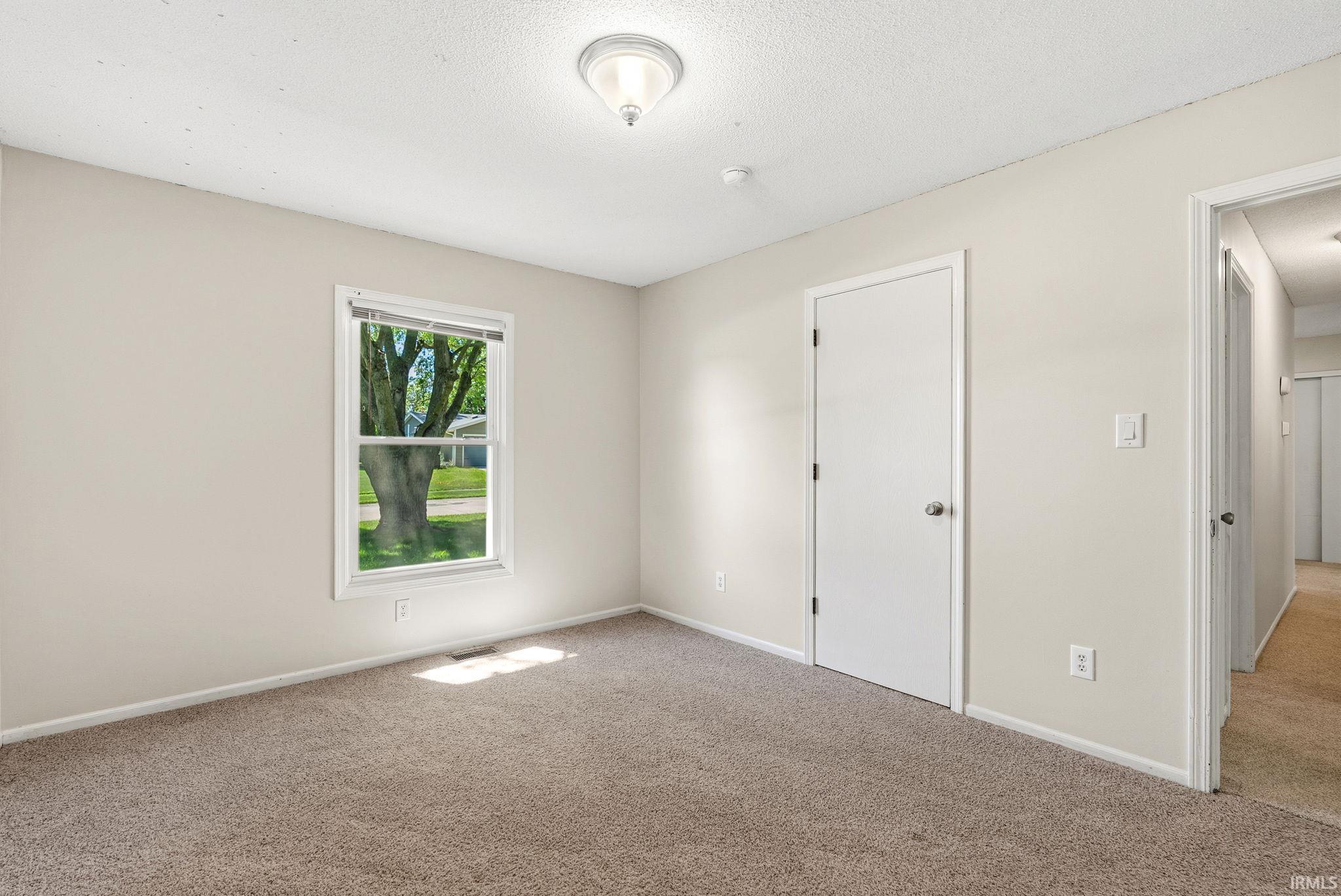 Carpeted room featuring a white-trimmed window, light neutral walls, and a white interior door