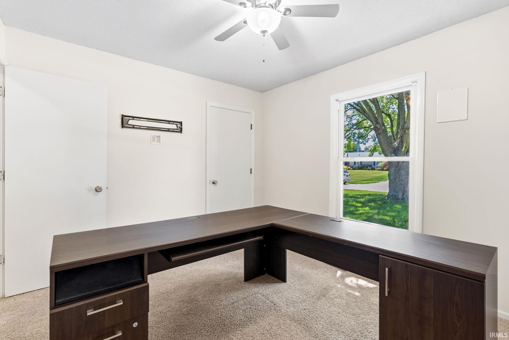 Room with light-colored carpeting, two white doors, a ceiling fan, and a window providing natural light