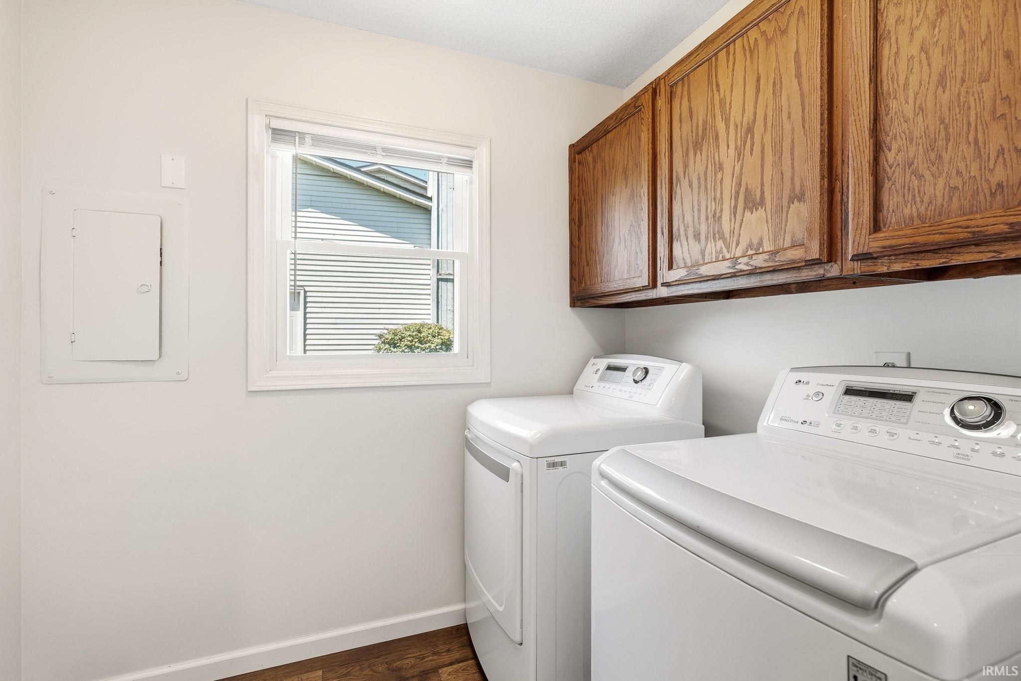Dedicated laundry space featuring rich wood-finish upper cabinetry, a window with natural light, and wood-finish flooring