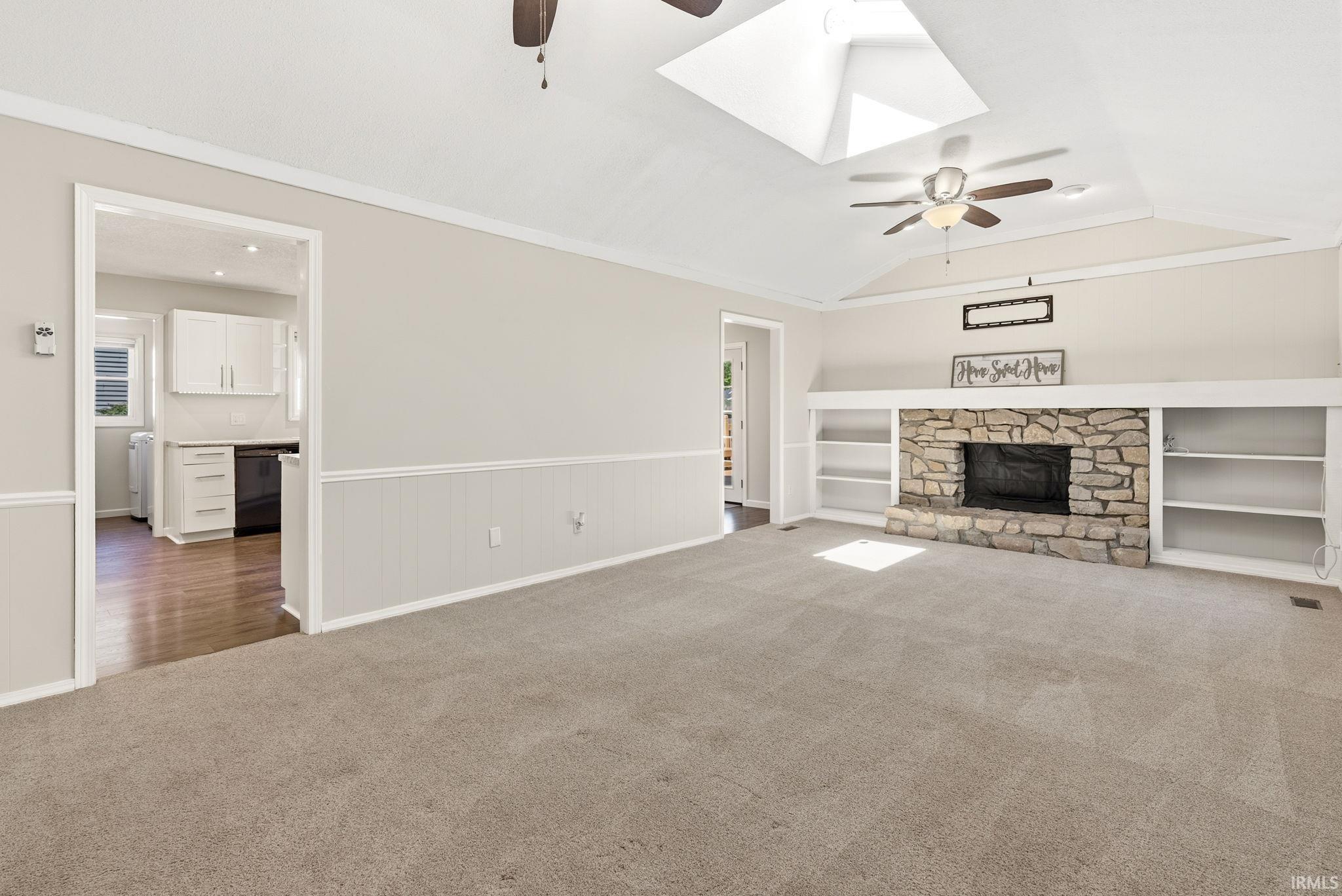 Spacious living area featuring a stone-clad fireplace with built-in shelving, vaulted ceilings, and skylights