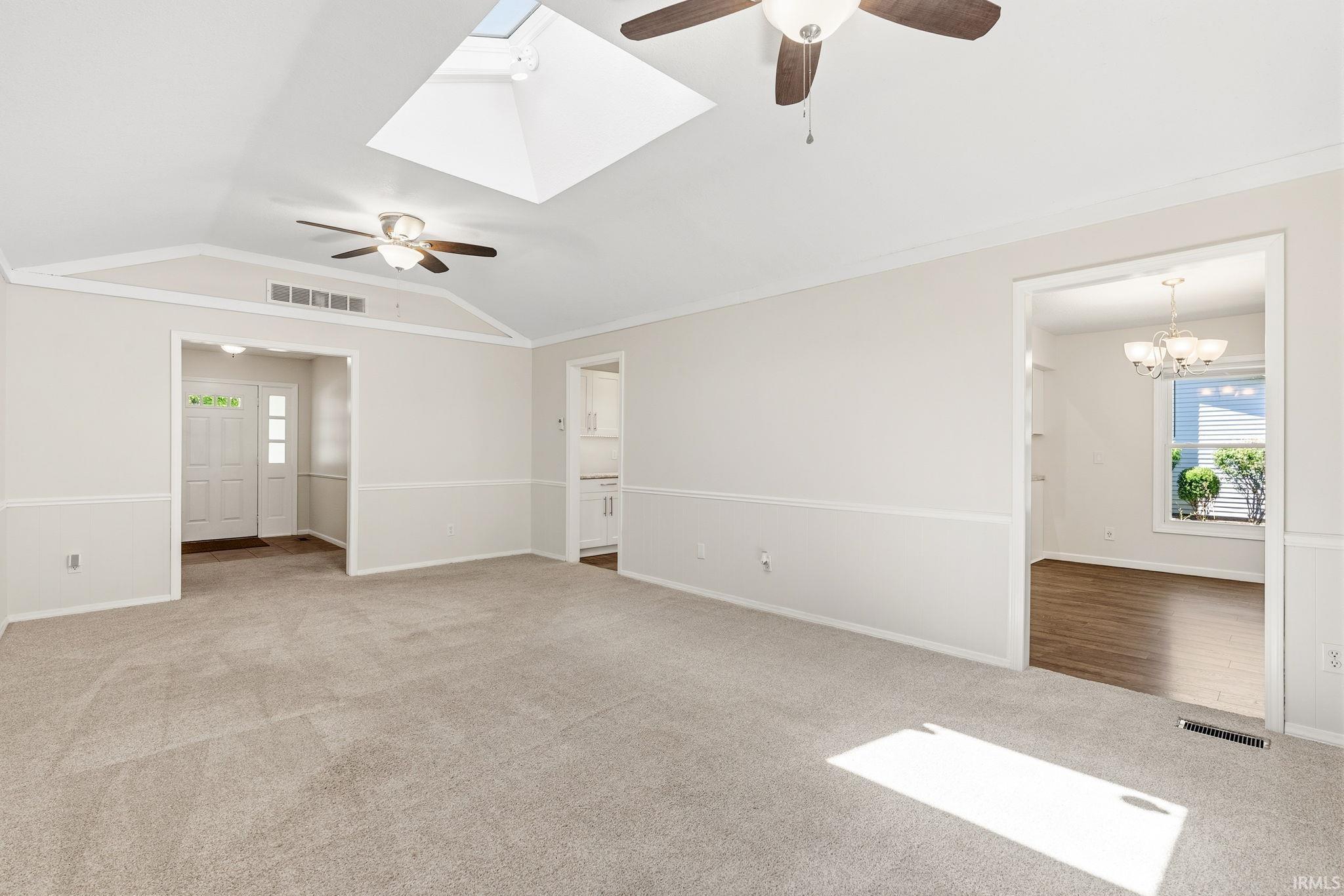 Expansive carpeted living area featuring vaulted ceilings, a skylight, and two ceiling fans