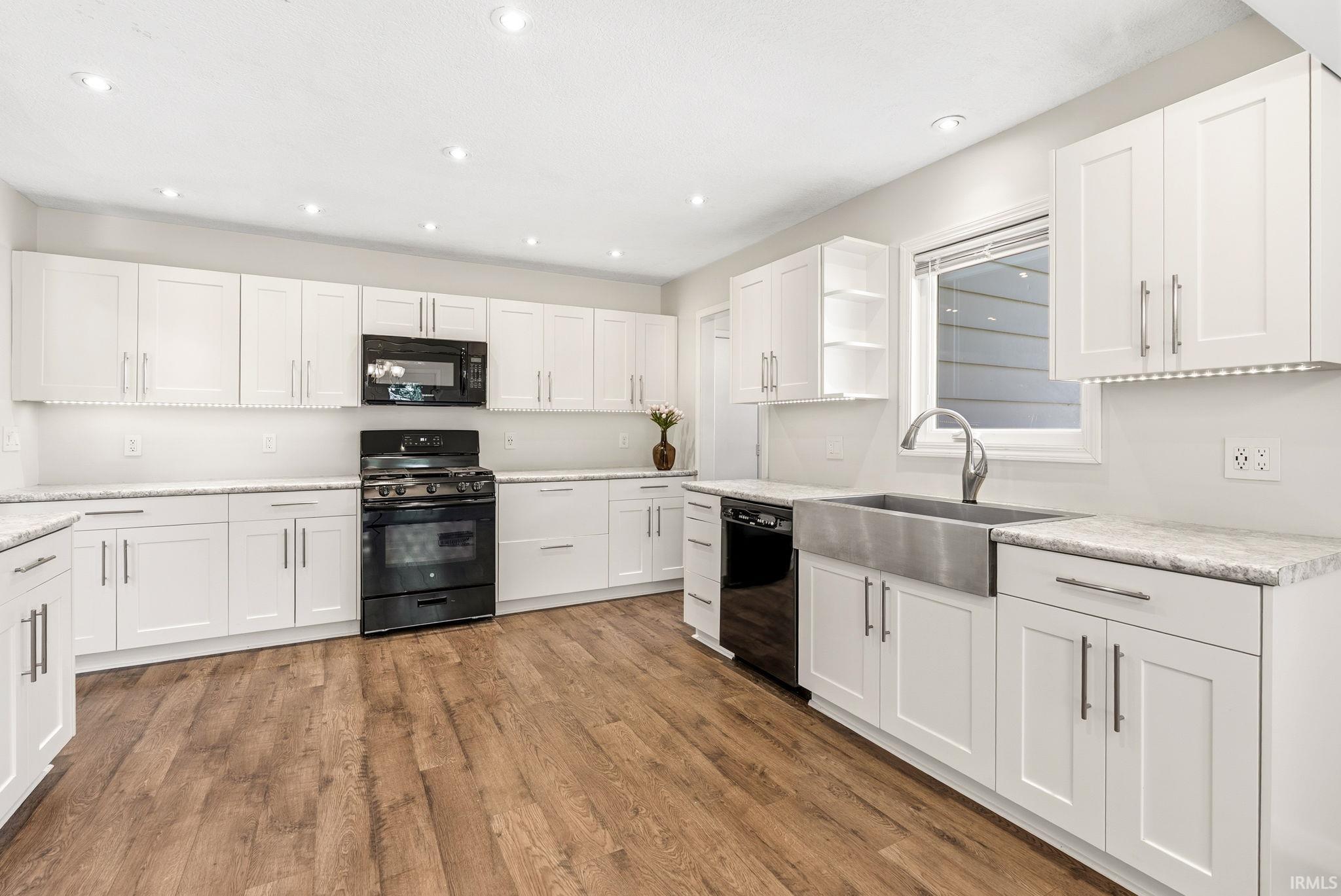 Kitchen featuring extensive white shaker cabinetry, light-toned countertops, wood-finish flooring, recessed lighting, and a stainless steel farmhouse-style sink with a pull-down faucet
