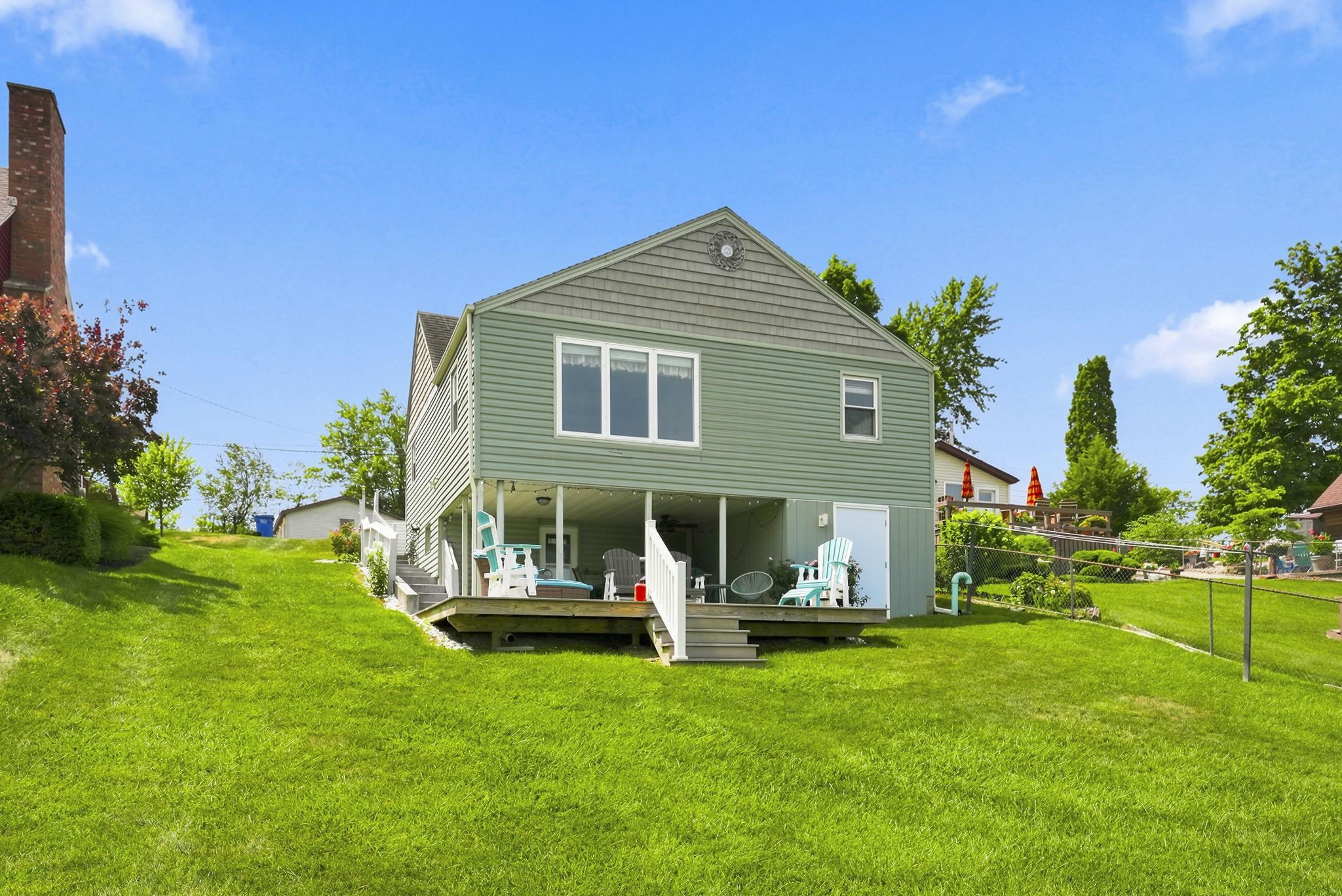 Rear exterior featuring green siding, a lower-level covered patio, new composite deck and expansive yard to waterfront