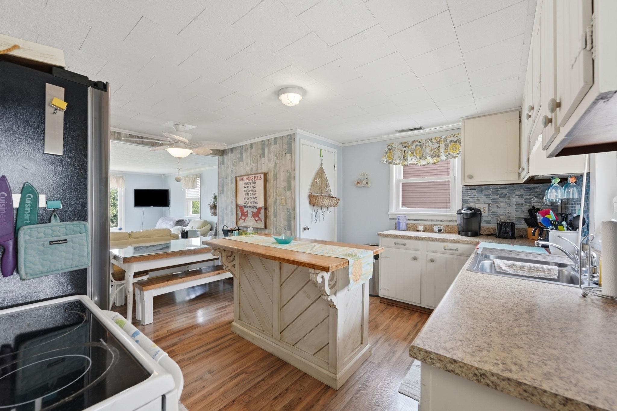 Open Kitchen featuring wood-finish flooring, light-toned countertops, white cabinetry, and a tile backsplash  All appliances, kitchen utensils and items on counter remain - house sold TurnKey