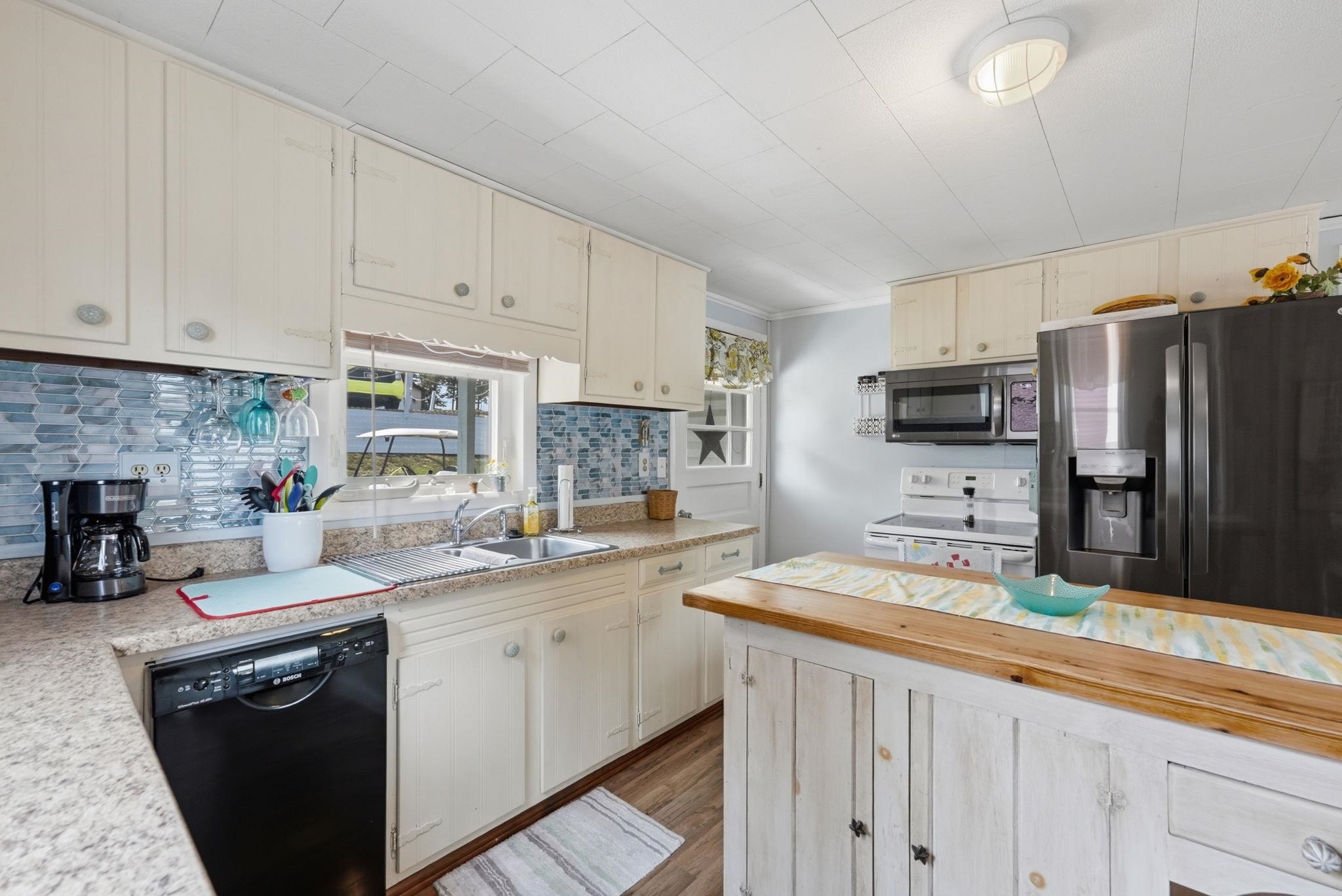 Kitchen featuring cream cabinetry, granite-style countertops, a blue glass tile backsplash, and a wood-finish island with storage