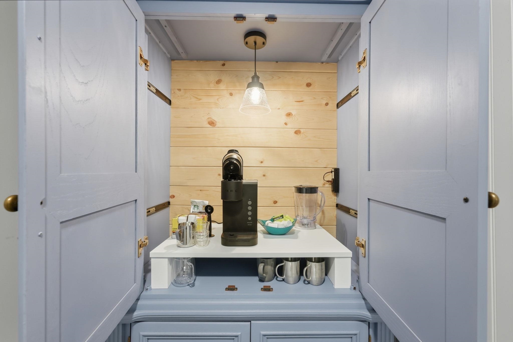 Free standing wood beverage station featuring light blue cabinetry, natural wood paneling, a suspended light fixture, and a white countertop perfect for those early morning lake days