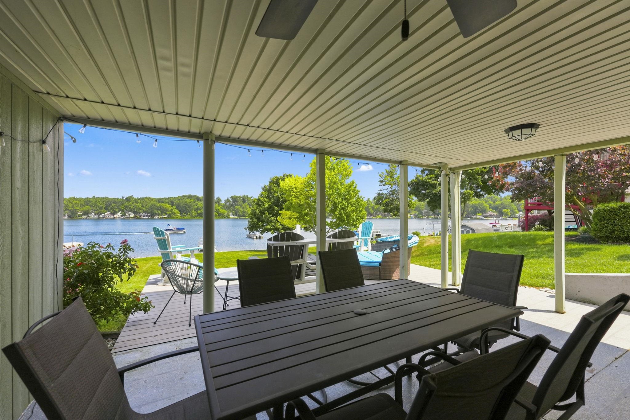 Covered patio with a planked ceiling, integrated lighting, ceiling fan and direct access to a waterfront lawn  Beautiful Panoramic Sunset Views await! PLUS, All outdoor furniture remains.