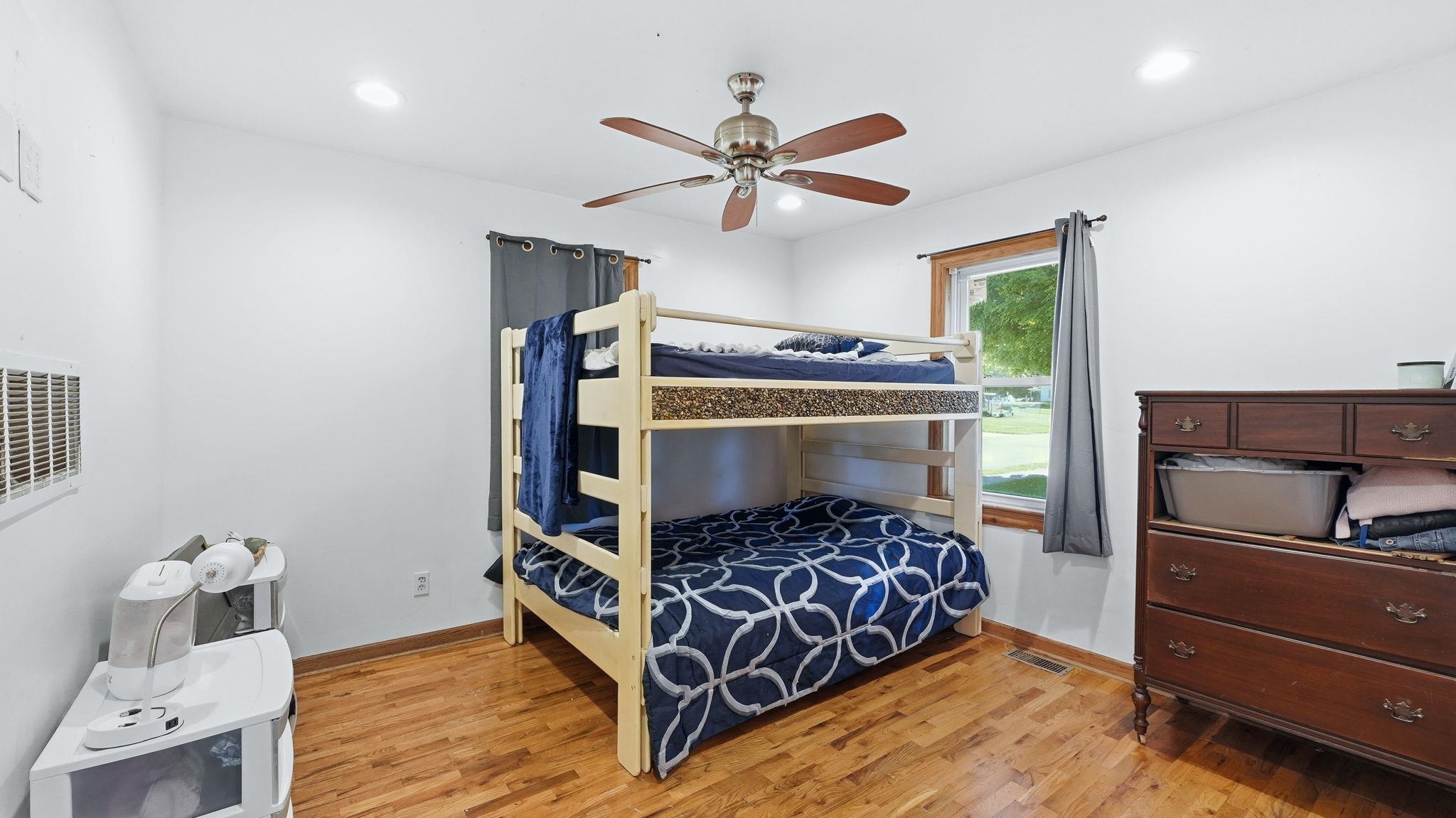 Hardwood flooring paired with white walls, a ceiling fan with integrated lighting, and a single window with wood trim