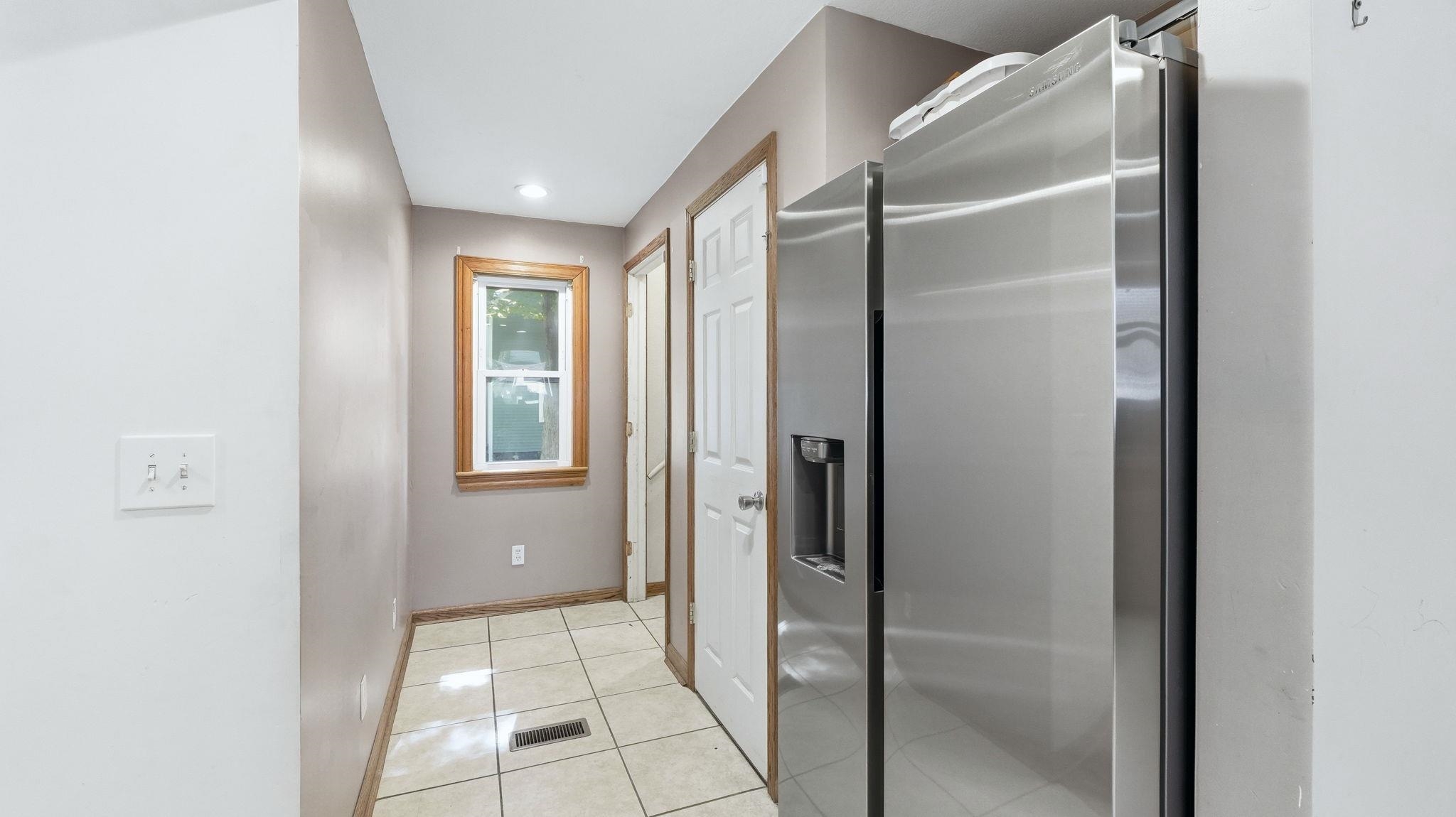 Stainless steel side-by-side refrigerator, recessed lighting, tile flooring, window with wood trim, and two white interior doors