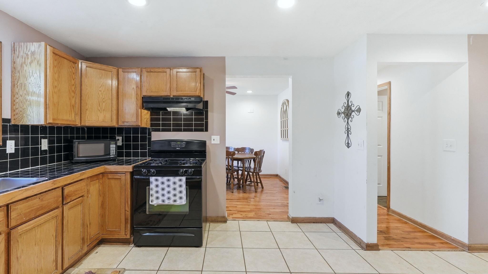 Kitchen featuring wood-finish cabinetry, black tile backsplash, and a black gas range