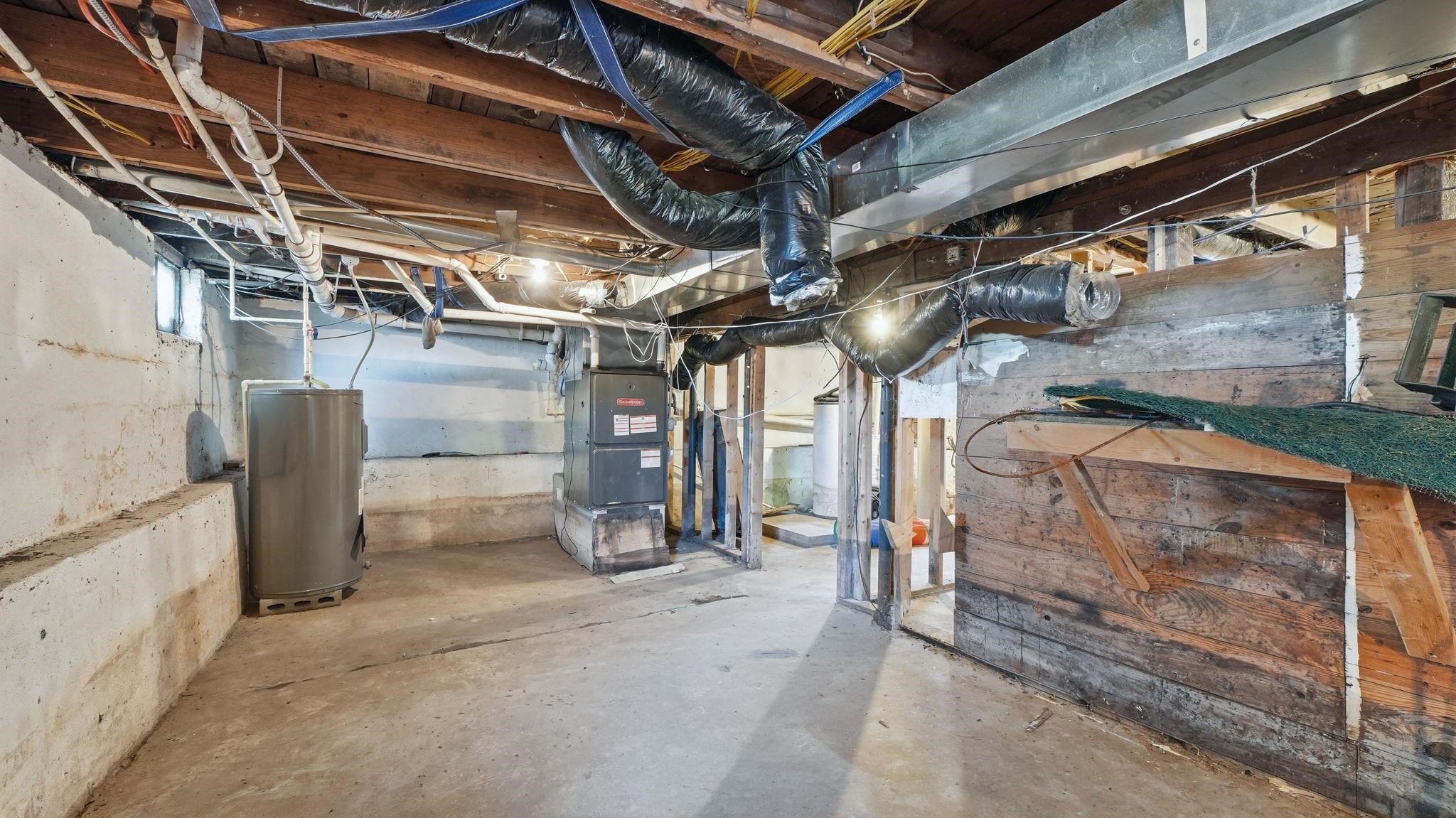 Unfinished basement featuring exposed wood joists, concrete flooring, a water heater, and a furnace unit