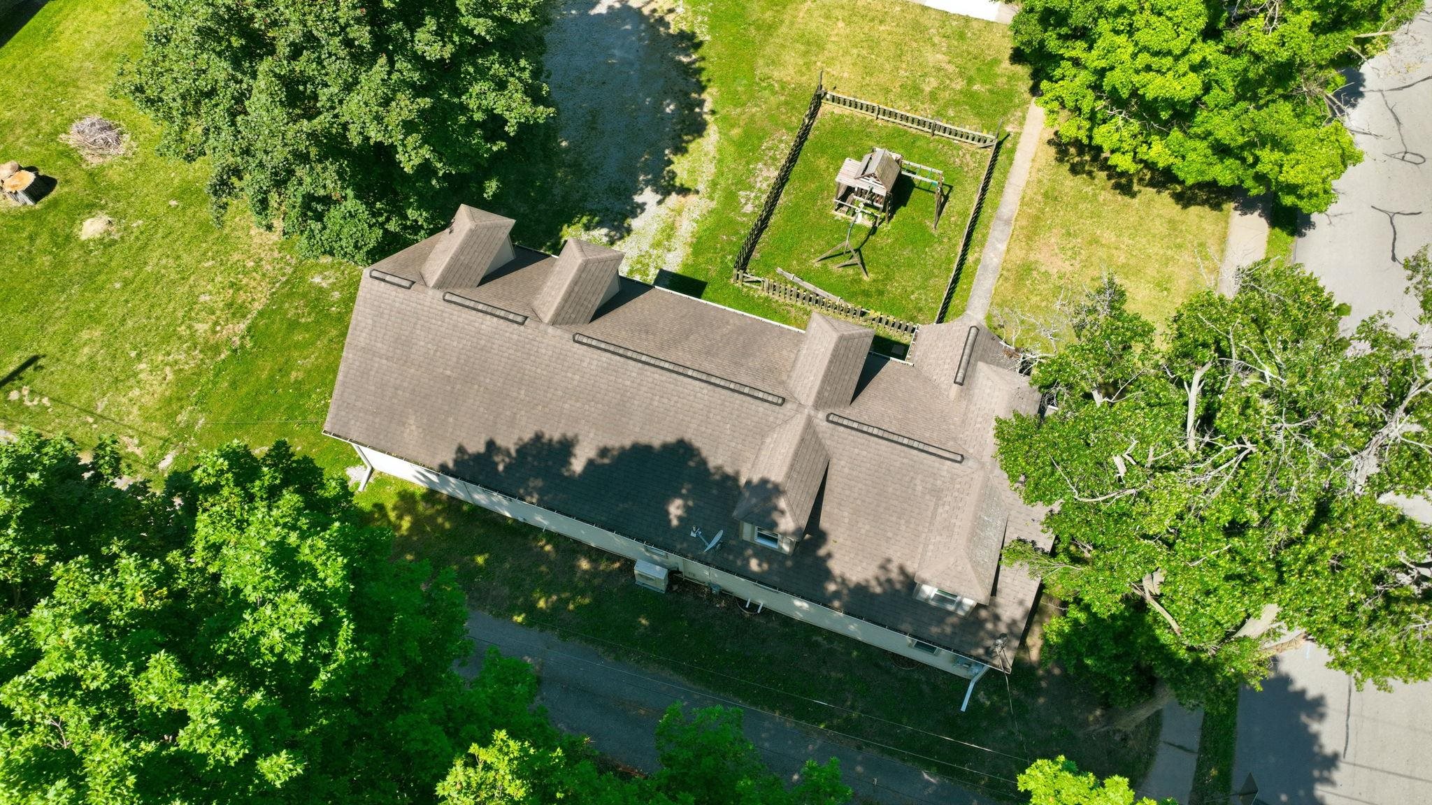 Gable roofline with multiple dormers, surrounded by mature trees and green space