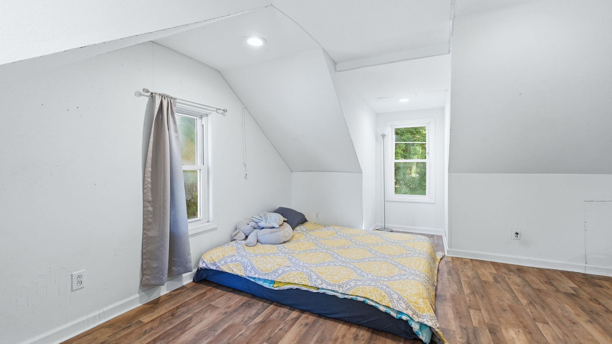 Vaulted ceiling room featuring wood-finish flooring and two single-pane windows