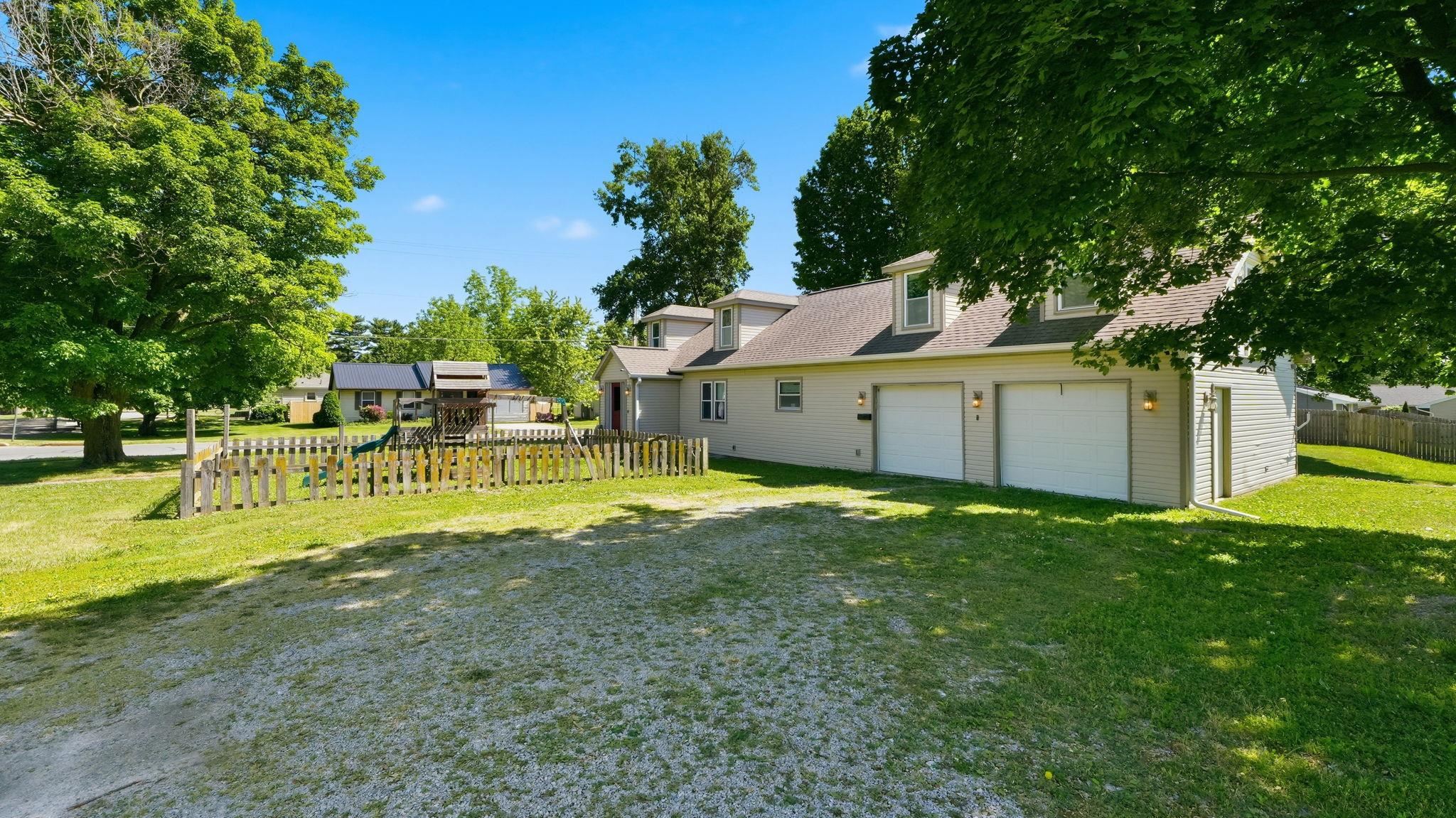 Gravel driveway fronting a property with light-colored siding, a multi-car garage, and dormer windows