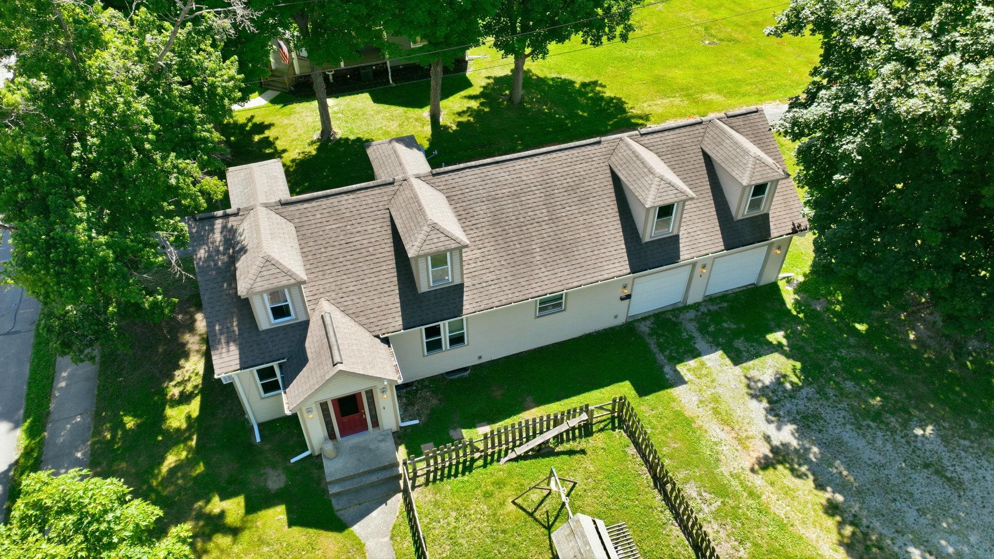Aerial perspective showcasing a property with a distinct roofline, multiple dormer windows, and an attached two-car garage