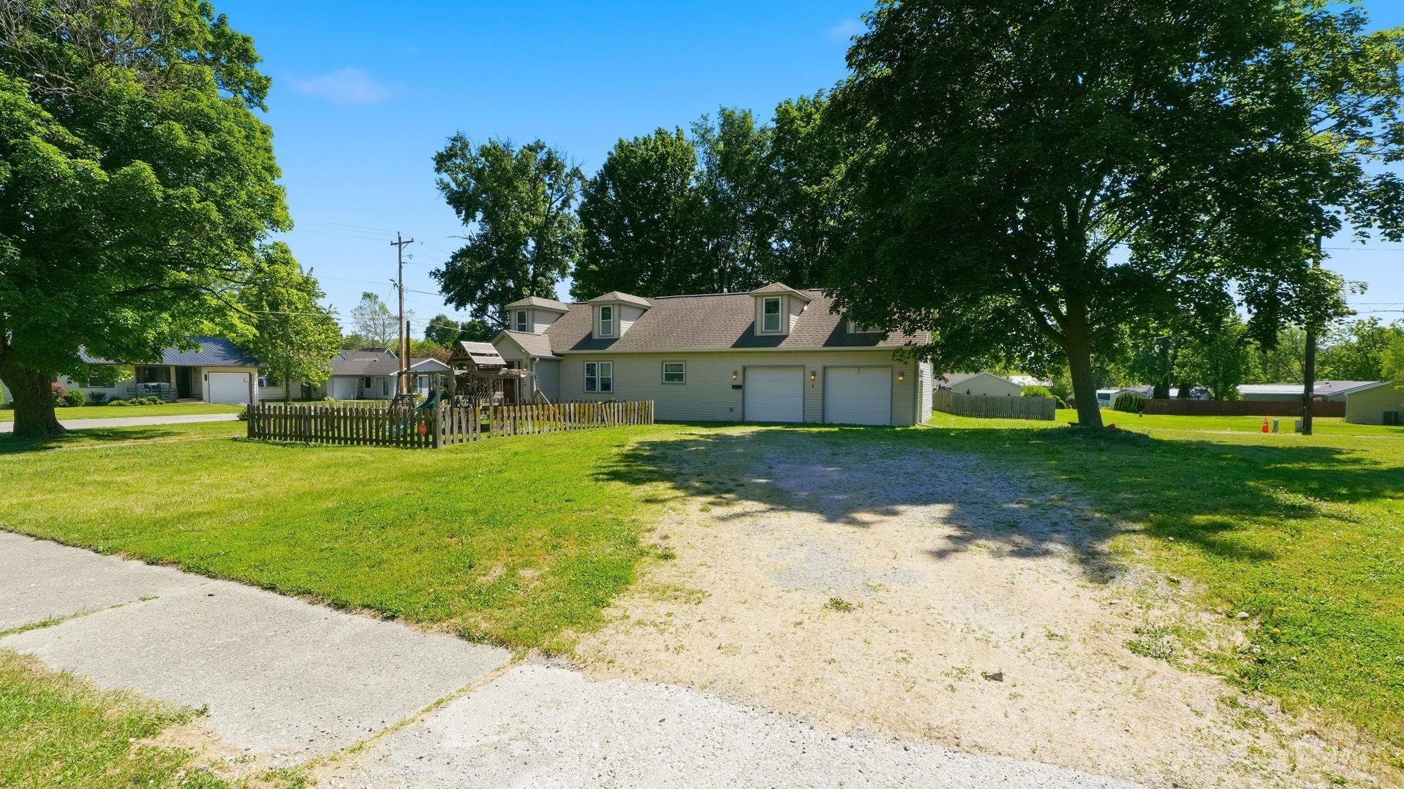 Property exterior featuring a beige facade, white garage doors, dormer windows, and a gravel driveway