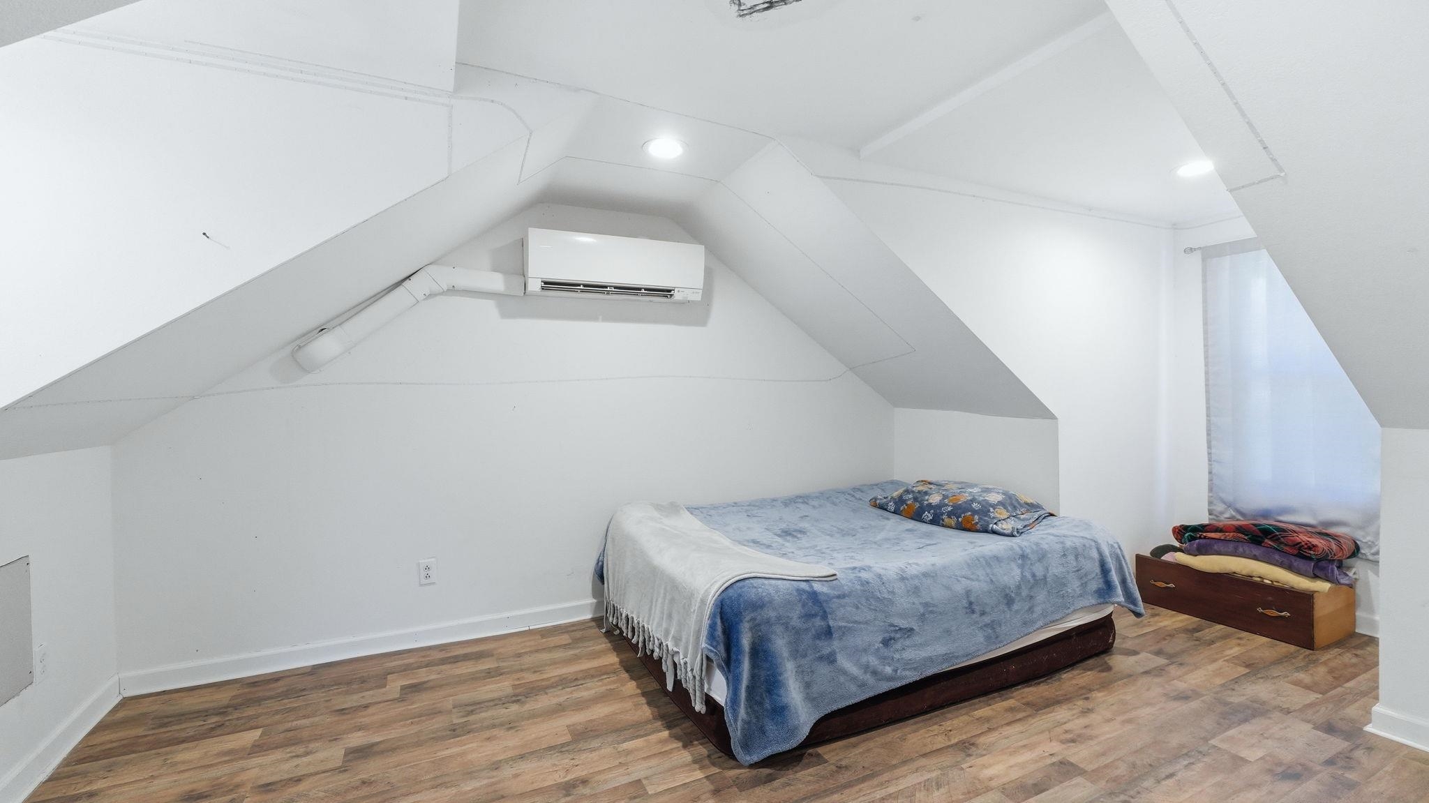Attic room featuring wood-finish flooring, white walls, and sloped ceilings