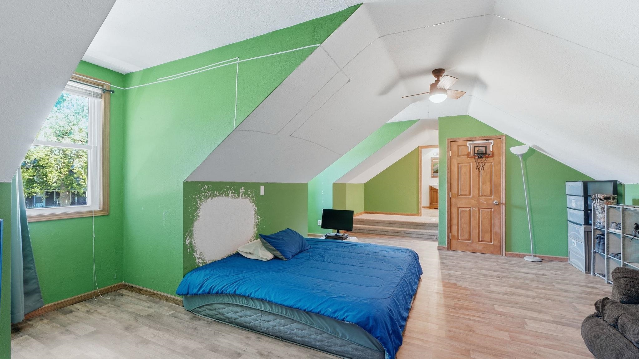 Attic space featuring wood-finish flooring, a window with wood trim, and a ceiling fan