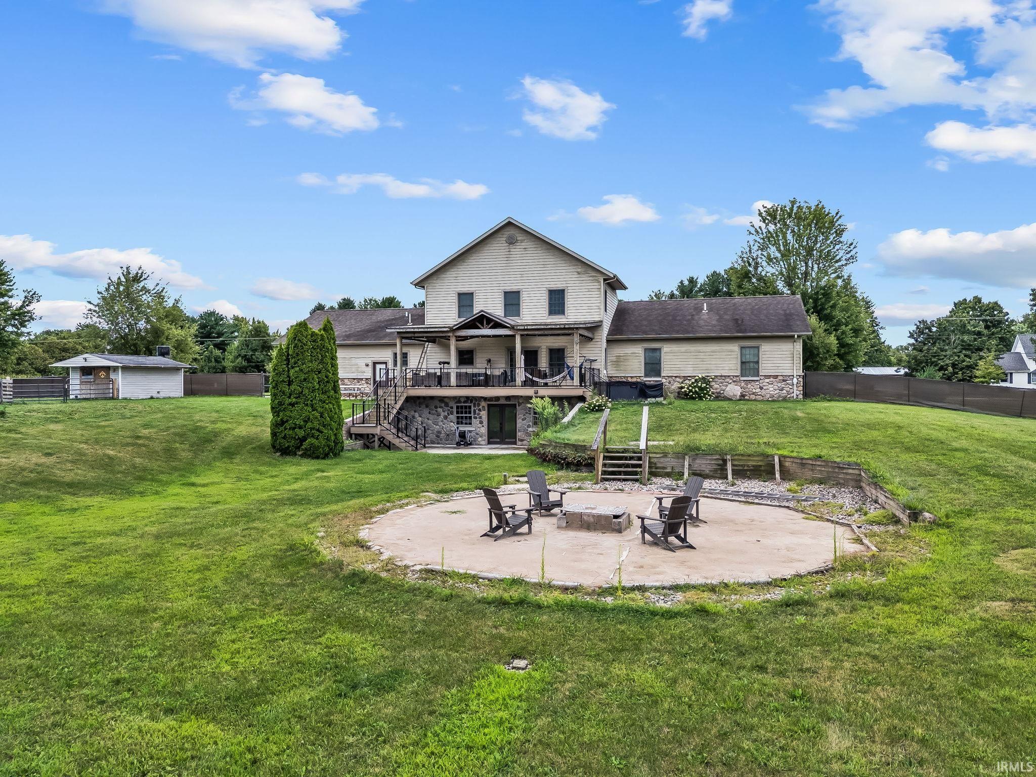 Expansive backyard featuring a circular stone fire pit, tiered landscaping with retaining walls, and a multi-level deck with a covered patio