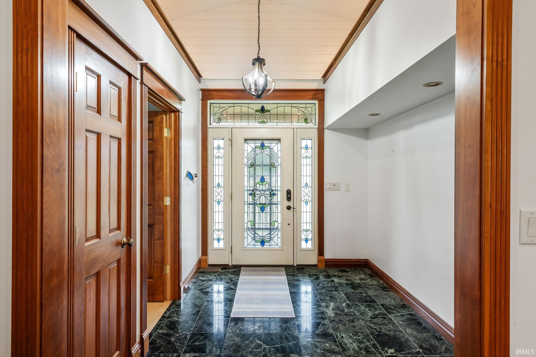 Entryway featuring a decorative stained-glass door with sidelights, a coordinating transom window, a dark stone tile floor, and rich wood trim