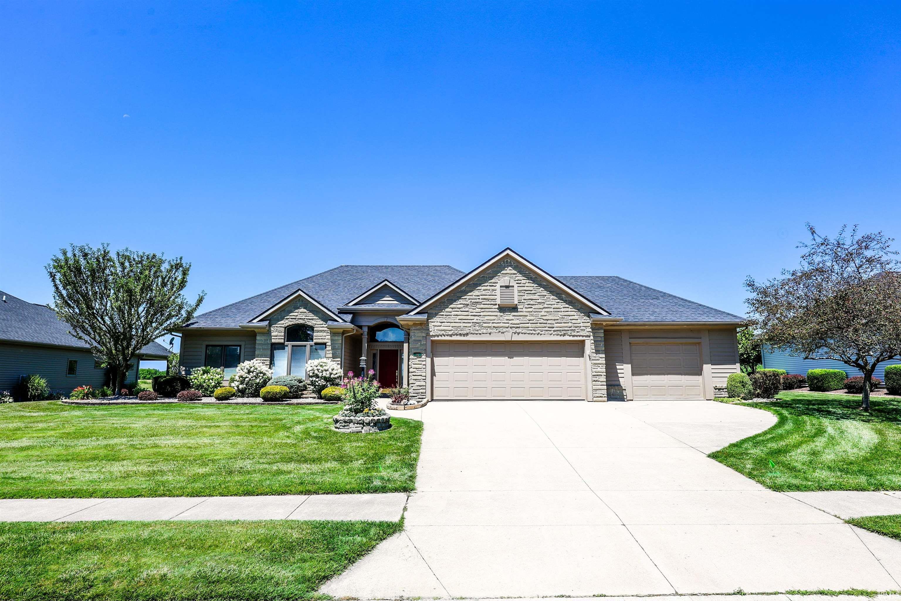 Stone facade residence featuring a multi-car garage, mature landscaping, and a paved driveway