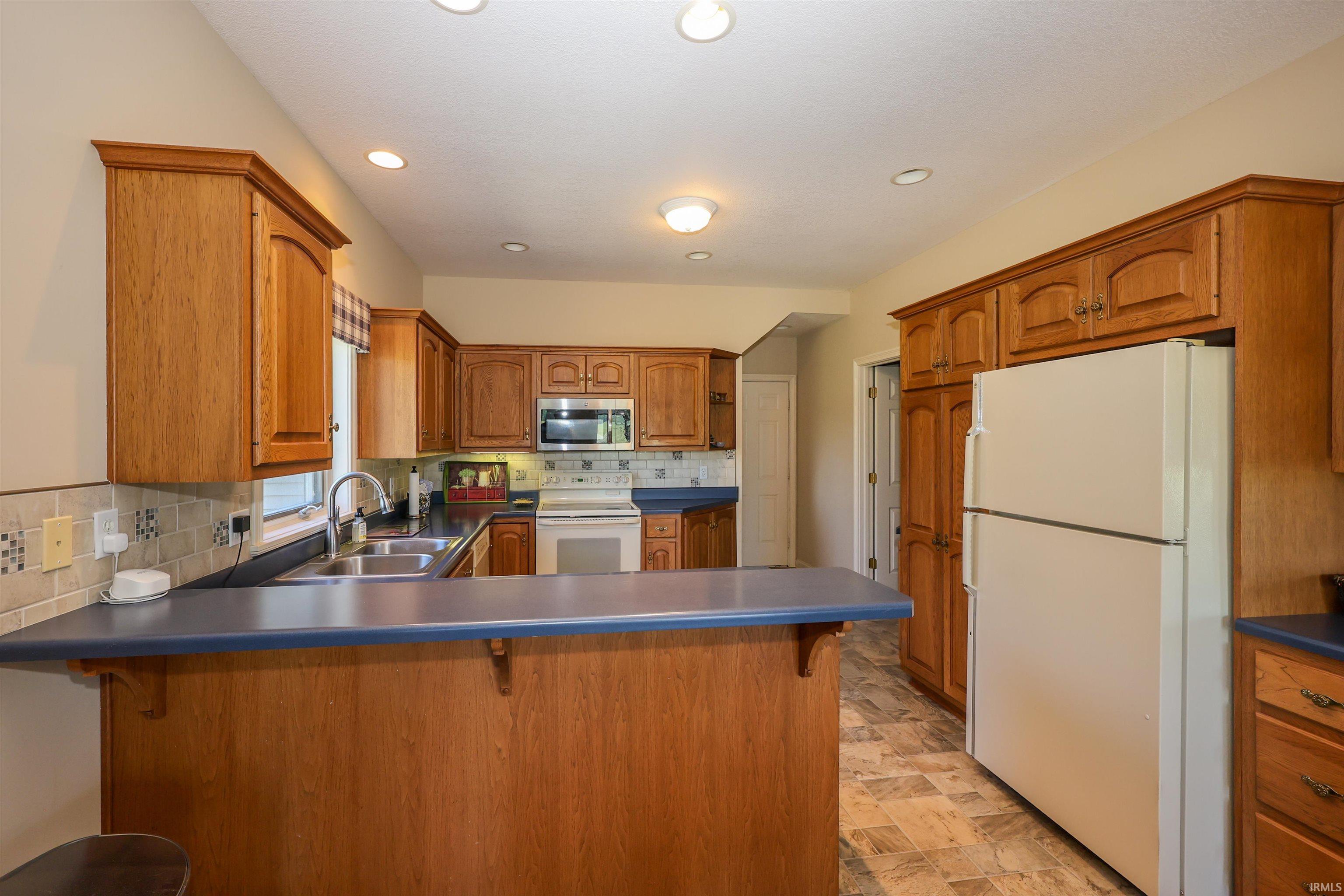 Kitchen featuring wood-finish cabinetry, a built-in microwave, a double basin sink, recessed lighting, and tile flooring