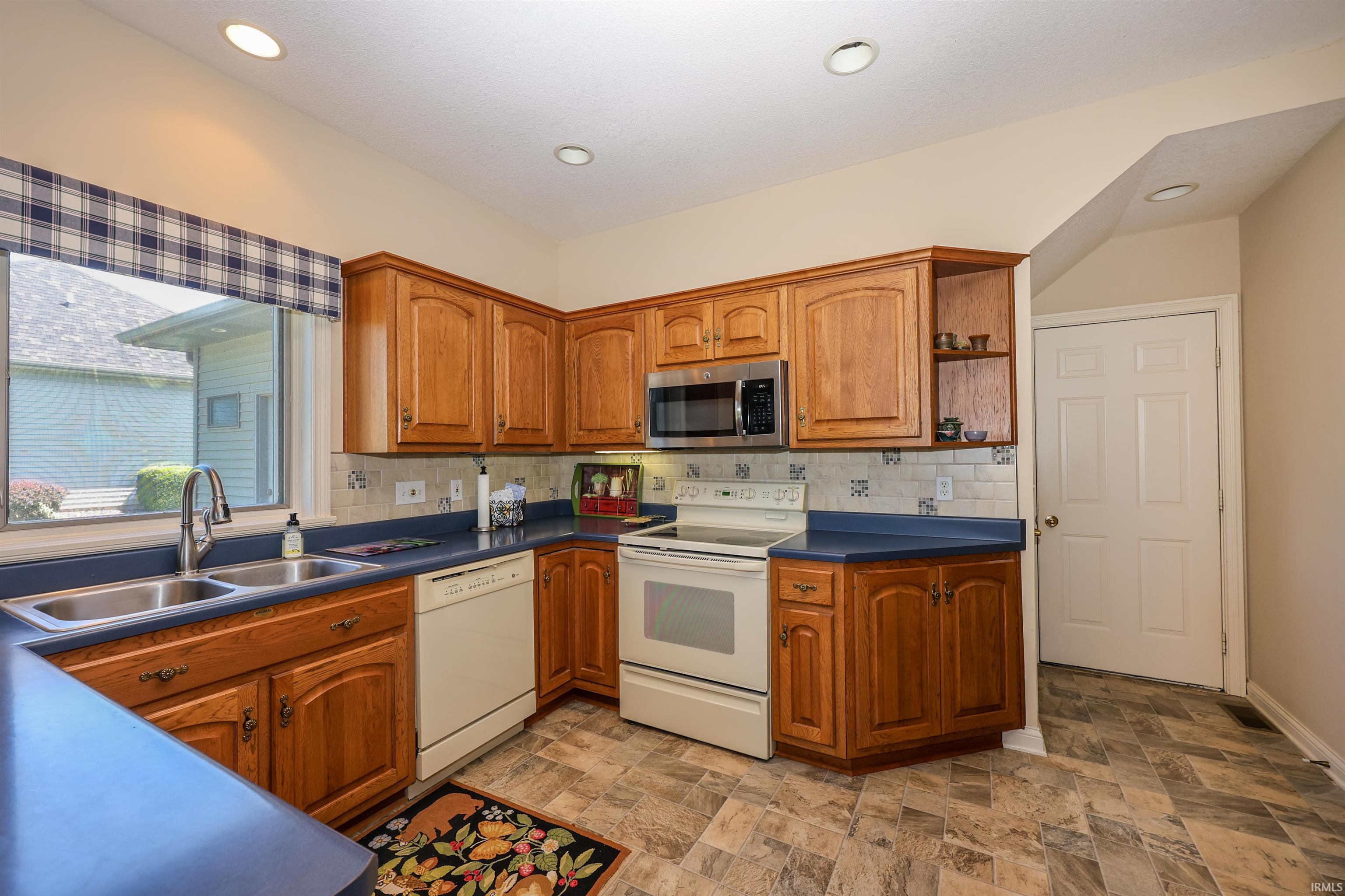 Kitchen featuring wood cabinetry, laminate countertops, stainless steel sink, white electric range, and microwave