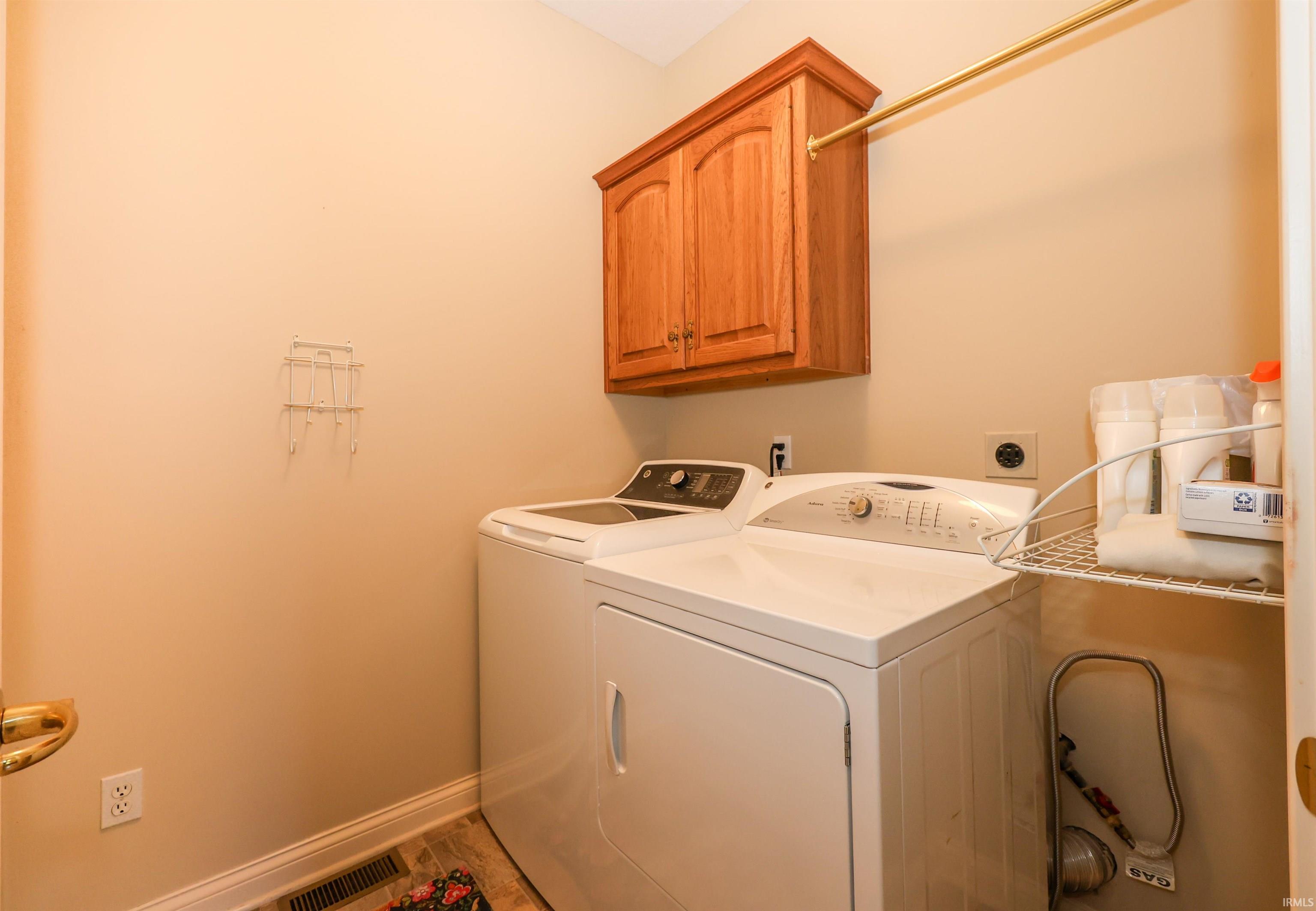 Dedicated laundry area featuring wood-finish cabinetry, a brass-toned hanging rod, and wall-mounted shelving for organization