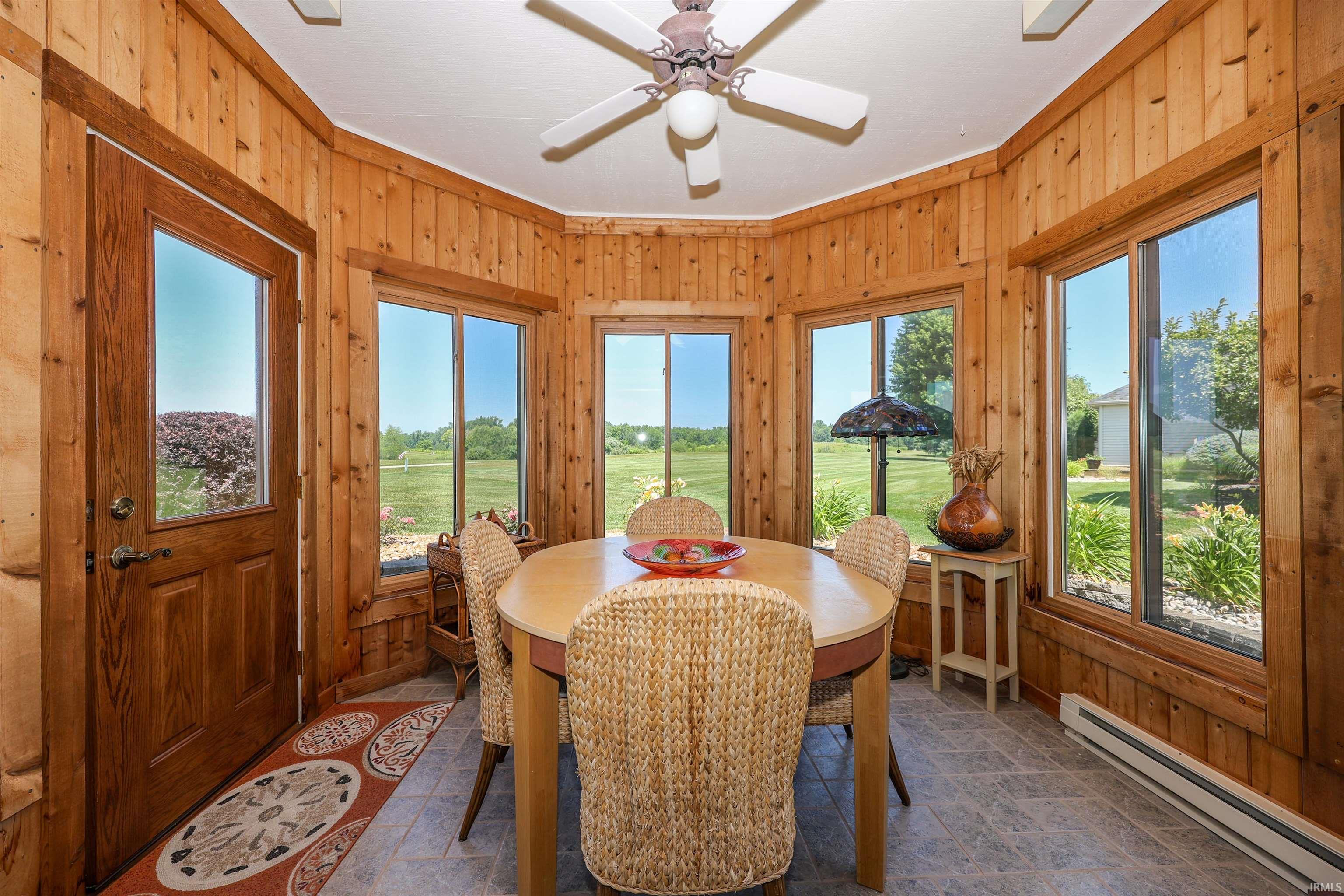 Sunroom featuring wood paneling, multiple windows, a ceiling fan, and tile flooring