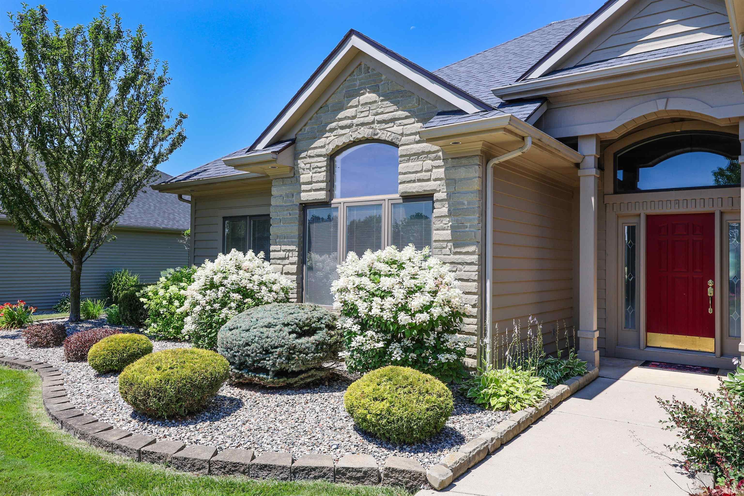 Stone facade entry featuring a distinctive arched window, a vibrant red entry door, and manicured landscaping with varied plantings