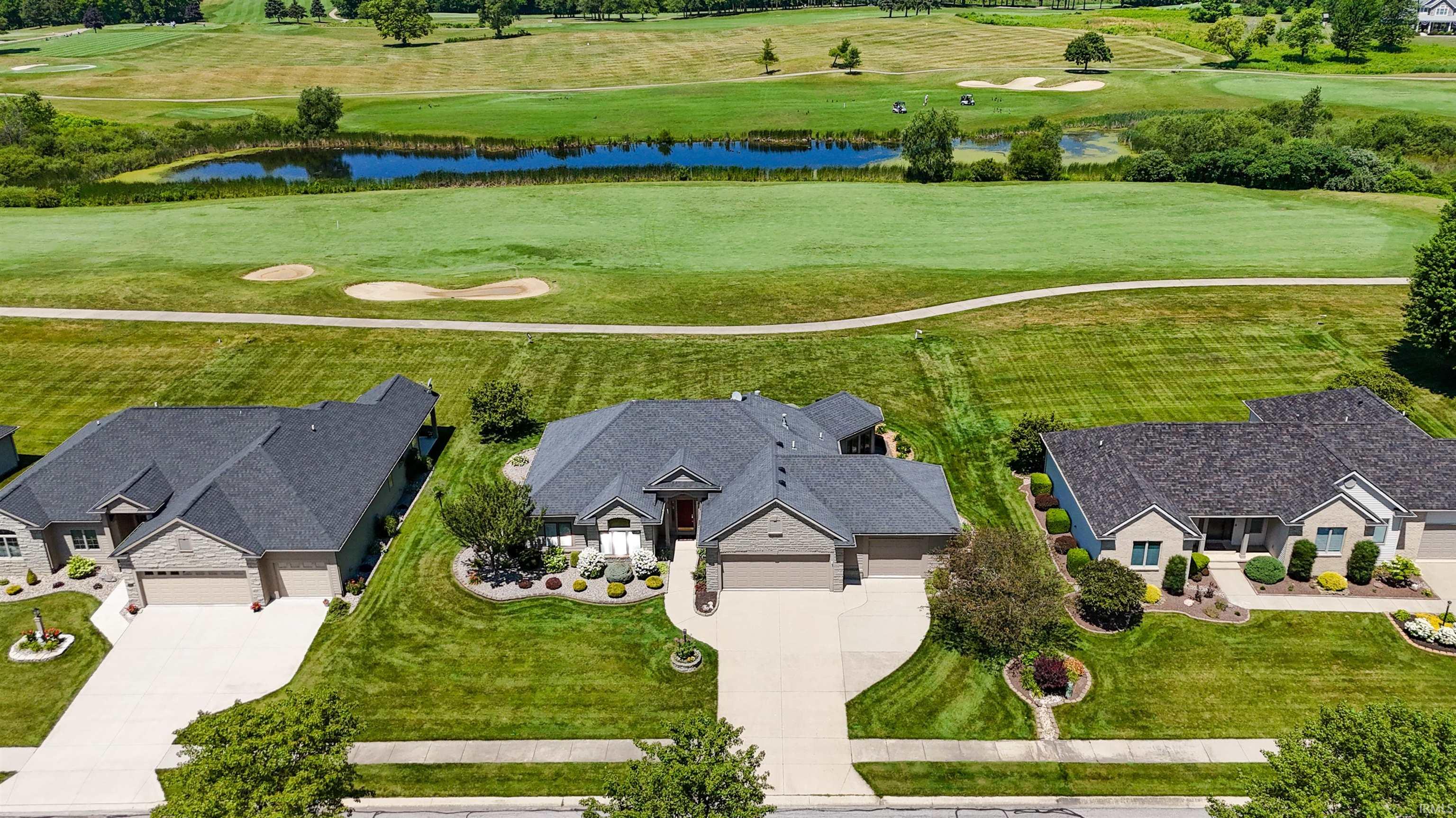 Overlooking a golf course with water features and sand traps, this property features a spacious lawn, mature landscaping, and an attached two-car garage