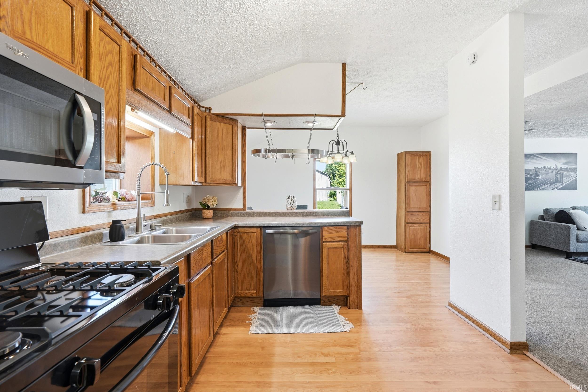 Kitchen featuring wood cabinetry, stainless steel appliances, a double basin sink, and wood-finish flooring